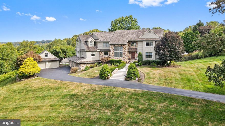 Nestled in the exclusive Blue Rock Meadows Community, this breathtaking four-bedroom, four-full and one-half bath Hazely Builders-built home is the height of luxury and refined living. Set on 4 private acres, this hilltop estate offers incredible views, an exceptional layout, and a backyard park style retreat all within minutes of West Chester’s vibrant downtown, scenic trails, local history and top-rated schools. French provincial meets cottage in this custom homes look and incredible architectural design. A long winding driveway brings you to a grand stepped entrance adorned by local quarried Pennsylvania brown field stone. This home welcomes you with soaring ceilings, a marble floored foyer, gleaming site finished hardwoods and an abundance of natural light. Designed for seamless entertaining and everyday comfort, the open-concept layout flows effortlessly from one elegant space to the next. The grand two-story formal living room features a wide 4 door French door with an incredible arched window above that saturates this room with light. An inviting fireplace with a 6 foot custom wood mantel shelf and overmantel to the ceiling is the centerpiece of this room filled with more stunning features than we can mention. A first floor bedroom with ensuite full bath and adjacent home office allow for flexible use with guests that can’t climb stairs. A two story dining room big enough for any family get together features another window over window beautifying this dining area for any holiday meal.  The heart of the home is the designer chef’s kitchen, a true showstopper with custom cherry cabinetry, premium granite countertops, Sub-Zero built-in refrigerator, double ovens and a cook top located on the oversized island. A huge walk-in kitchen pantry, kitchen secretary, laundry room, half bath, built-in wet bar and cozy morning room add warmth and versatility. The kitchen opens to a large family room with an attached vaulted sunroom with skylights and another arched window over window. The morning room opens through French doors to the expansive outdoor deck system which spans the length of this home and spills into an outdoor pool that belongs in a resort. The pool has been completely rebuilt in 2013 and provides a multi-level deck with separate spa with water fall into the main pool and trimmed out with more brown field stone and amazing landscaping. The second floor is anchored by the luxurious huge primary suite, a private retreat featuring a spacious sitting area, gas burning fireplace, a spa-like bath with a walk-in shower, soaking tub, separate water closet, two vanities and two oversized walk-in closets and more windows over windows with vaulted architectural ceilings. Cross the open hallway to two additional ample bedrooms that share a beautifully designed Jack-and-Jill bath. The lower level is an entertainer’s dream. Designed by Hazely Builders in 2019, the finished walkout basement includes tall ceilings, a guest suite, 5th bedroom, luxurious full bath, a 2nd kitchen with peninsula, dining area and another family room with electric fireplace for more family and friends entertaining. The lower level also provides access to a future wine room, mud room with a door to the rear yard and pool area and interior access to the attached 3 car garage. The outdoor living space is just as impressive as the interior, with a stone walk way around the home and to the pool and patio and the expansive deck system all surrounded by a beautifully manicured lawn, decorative landscaping, mature trees and horizon and wooded views as far as four acres can see. Whether hosting a summer barbecue or family wedding or enjoying a quiet evening under the stars, this outdoor retreat is truly exceptional. A detached two-car oversized garage, making a total of 5 full garage bays, features a future unfinished living area above and provides for plenty of car and sports activity storage adding both practicality and fun to an active lifestyle.