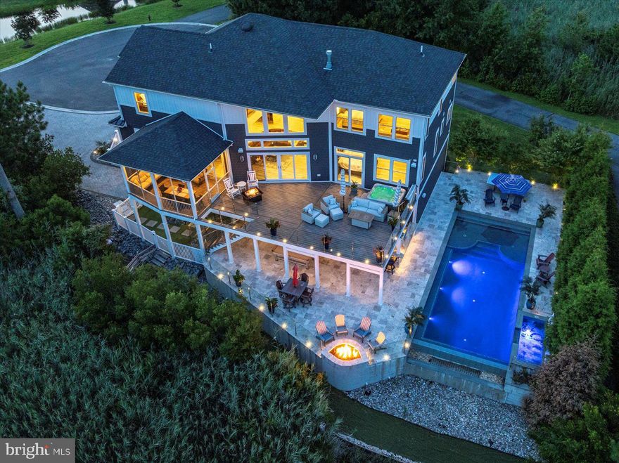 Waterfront Estate with Infinity Pool, Hot Tub & Deeded Boat Slip in Bay Point Plantation-Welcome to your dream coastal retreat in the exclusive community of Bay Point Plantation, where luxury meets lifestyle along the peaceful shoreline of a protected 142-acre nature reserve. Just minutes from Assateague Island, Ocean City beaches, and the charming town of Berlin, this stunning waterfront estate offers panoramic water views, high-end finishes, and resort-style amenities—including a deeded boat slip, custom infinity-edge pool, dual hot tubs, firepit, and expansive indoor-outdoor living and entertaining spaces. As you step through the front door, you’re immediately captivated by the wall of expansive windows and sliding glass doors that frame unobstructed views of the water, creating a seamless connection between indoor and outdoor living. The open-concept design flows effortlessly from the dramatic two-story living room, centered around a floor-to-ceiling fireplace, into the spacious dining area—perfect for hosting meals with family and friends while enjoying mesmerizing sunsets over the water. The heart of the home is a true chef’s kitchen, where style meets functionality. It features a large quartz-topped center island, a Viking gas cooktop, double wall ovens, custom cabinetry, beverage refrigerators, and an expansive walk-in pantry with built-in shelving and ample storage. A screened porch just off the dining area and a glass-railed upper deck further enhance the breathtaking water views and offer the perfect spaces for morning coffee or evening relaxation. The main-level owner’s suite is a private sanctuary with tranquil water views, two custom walk-in closets, and a luxurious en-suite bath featuring dual vanities, a freestanding soaking tub, a modern tiled shower, and heated tile floors. Step directly from the suite to the pool and patio through your private entrance, where lush tropical landscaping brings the outdoors in and creates a truly serene experience. This level also includes a beautifully designed home office, a spacious laundry room, and a stylish half bath. Upstairs, the home continues to impress with three generously sized bedrooms, each filled with natural light and offering views and privacy. One bedroom features its own private en-suite bath and can be a 2nd primary suite, while the other two bedroom share a well-appointed Jack-and-Jill bath. Whether you take the grand staircase with sleek cable railing or the private elevator, the upper level offers comfort and privacy for family and guests alike. The ground floor is dedicated entirely to entertainment and relaxation. Here you’ll find a state-of-the-art theater room—complete with a Murphy bed for use as a fifth bedroom if desired—a spacious game room, a fully equipped bar, and a second kitchen that opens directly to the elevated back patio. A full bathroom on this level adds convenience, while direct access to the outdoor living area ensures seamless entertaining. Step outside into your private waterfront oasis, where a custom infinity-edge pool, two hot tubs, and breathtaking bay views await. The outdoor entertaining space includes a fully equipped kitchen with grill, refrigerator, kegerator, and crab pot burner, along with a covered pool table area, fire pit, mounted TV, and multiple dining and lounge areas ideal for crab feasts, barbecues, and gatherings both day and night. Additional highlights include a large two-car garage, ample guest parking, professional landscaping, and meticulous maintenance throughout the home. Bay Point Plantation offers residents access to nature trails, a private marina, and a quiet, coastal atmosphere surrounded by preserved natural beauty. This extraordinary home is more than just a residence—it’s a lifestyle. Don’t miss this rare opportunity to own one of the area’s finest waterfront properties. Schedule your private tour today and experience luxury coastal living at its absolute best.