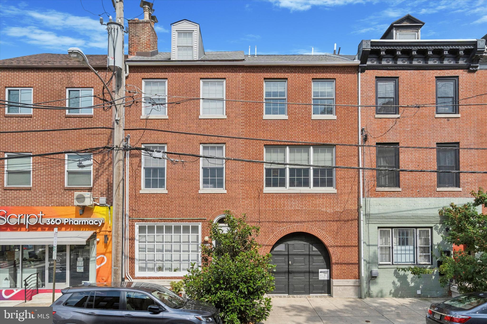 Welcome to 603 South 10th Street. Ideally situated between Bella Vista and Washington Square West, this light filled, double-wide duplex has been expanded to over 4300 square feet, with a 4BR, 3.5BA and a 1BR/1BA apartment, RM1 Zoning with Duplex Use Permit) on the first floor, a total of 5 bedrooms and 4.5 baths. Meticulously maintained by its owner, The oversized 3 car garage, 3 gorgeous outdoor spaces, an elevator, and tax abatement makes this property truly stand out.
One flight up leads to the main level where you will find an expansive open floor plan that beautifully blends the original home with the addition completed in 2016. The huge family room with a tray ceiling and recessed lighting, hardwood floors and three large windows opening to 10th street. Access the elevated Ipe deck with pergola overlooking the park-like backyard with mature specimen trees, a large bluestone slate patio and raised planted beds. The renovated eat-in kitchen features pristine white cabinetry, stone countertops and side island, stainless appliances, glass tile backsplash, pantry and a convenient half bath. The adjacent dining room has a cedar tray ceiling with cove lighting and hanging pendant tracks and opens to the elegant living room with a white marble gas fireplace flanked by floating wood shelves on either side. Continue upstairs to find the primary suite with a sitting room at its entry. The ample sized bedroom has hardwood flooring and a cedar ceiling with recessed lighting, an arched wood burning fireplace with colorful tiles and a red brick hearth and a large walk-in closet. The primary bath has a frameless glass stall shower tiled with inset nooks, corner shelves and a stone bench, granite vanities with double sinks and a linen closet. Two additional bedrooms, one currently serving as an office and a full bathroom in the hall. On the upper level there is a light filled open space with a dramatic arched entry which could be utilized as you please or enclosed to make a 4th bedroom with its own full bathroom. The relaxing DuraTec roof deck with raised planters is made for your enjoyment and completes the upper level.
On the ground level, there is a large 1 bedroom apartment that has a renovated kitchen with stainless steel appliances and granite countertops, two mini-split wall mounted A/C units and an in-unit washer and dryer. The unit has been continuously rented since 2016 and is currently occupied at 1600/month through July 2025. This is a great space that could be utilized as a guest suite, rental unit or easily modified to make this property a single family residence. Lease documents and apartment photos are available for review.