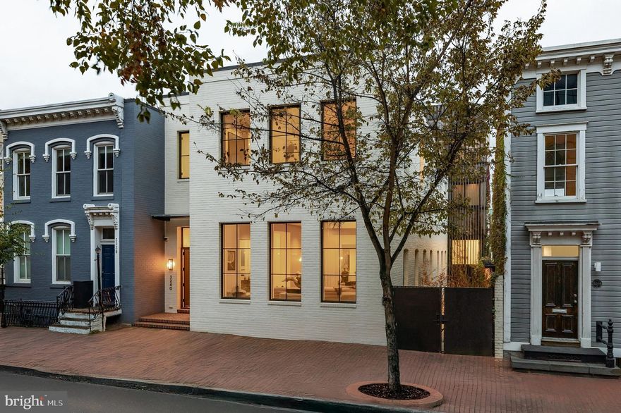 Commanding a premier location in the heart of Georgetown’s coveted West Village, 3240 Prospect Street NW is a rare offering of scale, sophistication, and versatility. Seamlessly integrating residential, commercial, and hospitality-grade amenities, the property is an architectural statement without equal in Washington.

A visionary collaboration between Muse | Kirwan Architects, Horizon Builders, and Arentz Landscape Architects, the home is at once an entertainer’s dream, a high-tech workplace, and a serene urban retreat.

From the street, the minimalist façade is understated yet striking, white brick cladding contrasts with dark, steel-framed Hope windows and doors. A discreet vestibule opens to a formal reception area, introducing a truly extraordinary floor plan spanning over 13,000 square feet, a scale virtually unheard of in Georgetown. An open sightline of more than 100 feet extends the full depth of the main level, amplified by soaring 11-foot ceilings.

The 41-foot reception hall and 26-foot formal dining room are bathed in natural light from a continuous wall of windows, setting the stage for grand entertaining. Limestone walls and herringbone floors evoke timeless elegance, while a gallery space features a fully equipped wet bar with an illuminated onyx backdrop. The formal living room transforms into a private lounge, complete with integrated lighting, sound, and even a fog machine. French doors open to a string-lit patio with water features, a bar, and an outdoor kitchen, extending the experience seamlessly outdoors.

The second level offers more intimate living spaces, anchored by an open-concept kitchen and family room. The kitchen is a chef’s dream, boasting a custom stainless-steel hood, a commercial-grade Thermador range, and integrated Sub-Zero, Wolf, and Miele appliances. High-gloss cabinetry and marble countertops complete the sleek, modern aesthetic. A leathered granite fireplace wall adds warmth to the adjacent family room. A private rear terrace offers panoramic views of Rosslyn’s skyline.

A central library lined with built-ins leads to a private office, both offering quiet, refined spaces. The front-facing primary suite overlooks Prospect Street and includes a spa-inspired bath with white marble finishes, a wet room, and a freestanding tub. The boutique-style dressing room, secured by biometric access, features a makeup station, center island, and custom illuminated cabinetry.

The top-level houses five additional bedrooms and four beautifully appointed baths, all designed for comfort and privacy.

Perhaps most extraordinary is the separately accessed lower level, a fully equipped professional office space. Designed for high-level functionality, it includes commercial-grade A/V, three glass-enclosed conference rooms, three executive offices, open workstations, a break room, two powder rooms, and a private garage with additional outdoor parking.

The home’s systems rival those of commercial buildings: a green roof, full Crestron smart home automation, Lutron lighting, automatic shades, integrated surround sound, intercom, biometric entry, 30+ surveillance cameras, fire suppression, and a private elevator serving all floors.

Just a block from M Street and Wisconsin Avenue, and directly across from Café Milano, this location is among the most prestigious in the nation’s capital. A seamless fusion of minimalist design, contemporary technology, and uncompromising elegance, 3240 Prospect Street NW is a singular residence in the Capital Region.