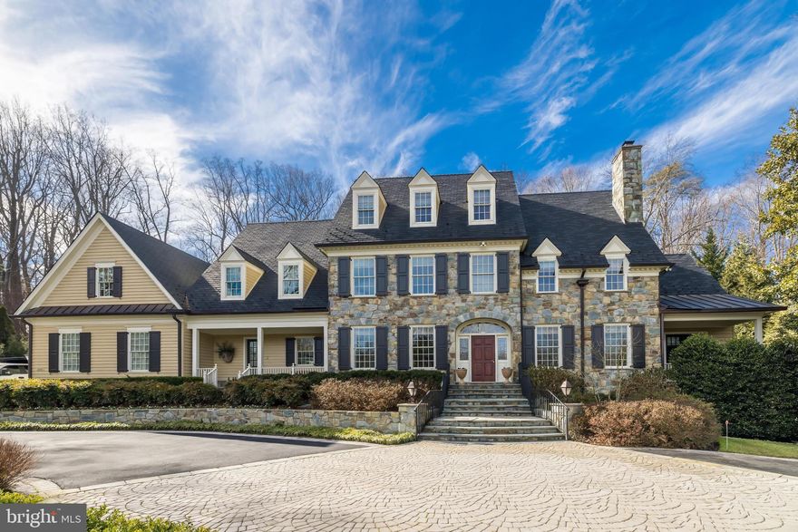 Originally conceived in 2002 through the distinguished collaboration of Buchanan Price and Michael Bowman, this stately New England-style colonial in Langley Forest commands an exquisite one-acre hilltop setting. Enveloped by mature, meticulously designed landscaping and extensive hardscaping, the estate is approached via a sweeping circular drive, evoking the timeless grandeur of a century-old manor. Designed for both lavish entertaining and effortless everyday living, this home seamlessly blends classic elegance with modern refinement.
Spanning approximately 10,000 square feet, the residence unfolds across a thoughtfully designed floor plan, encompassing six bedrooms, five full baths, two half baths, five fireplaces, and a three-car garage. Upon entry, designer lighting by Niermann Weeks and wall coverings by de Gourney, set the tone for an elevated experience. Interior designer Anne Dutcher's impeccable vision is reflected in every space, incorporating exclusive-to-the-trade finishes and distinguished design elements from Schumacher, Phillip Jeffries, and Conrad. Custom, furniture-grade built-ins, handcrafted by renowned cabinetmaker Michael Bruner, enhance the home’s functionality and timeless appeal. Over the past decade, the property has undergone a series of elegant enhancements, elevating the kitchen, all baths, and the walnut-paneled library to meet the highest of standards.
The chef’s kitchen is a masterpiece of craftsmanship, featuring bespoke cabinetry, a striking stainless-steel island with rivet detailing, hand-forged iron hardware, and top-tier appliances from Wolf, Miele, and Sub-Zero. Rohl fixtures lend an extra touch of refinement, while an adjacent bayed breakfast alcove—framed by floor-to-ceiling windows and crowned with a hand-painted ceiling by Artifice—welcomes natural light, fostering a warm and inviting ambiance. The adjoining family room, centered around a magnificent stone masonry fireplace, offers a seamless indoor-outdoor flow, with multiple French doors leading to the estate’s serene grounds.
A dual staircase ascends to the upper level, where wide hallways provide tranquil views of the surrounding landscape. The primary suite is a sanctuary of indulgence, accessed through a vestibule and enhanced by an additional ceiling by Artifice, a sitting room with fireplace, and a extensive walk-in closet. The spa-like en-suite bath is appointed with Waterworks fixtures, a steam shower, heated floors, and towel warmers, while the secondary bedrooms and baths showcase the finest materials and finishes, ensuring both comfort and elegance.
The lower level is an entertainer’s dream, featuring dual recreation spaces, a fully equipped bar, reclaimed white oak Gristmill hardwood flooring adding warmth and character to the space. The Lisa and Michael Weiss-designed, 1,500-bottle wine cellar offers an impeccable environment for collectors. Adjacent to a side door entry is an expansive laundry room with double units, bespoke cabinetry, a full renovated bath and a private Au Pair or in-law suite. 
Both the main and lower levels open to the estate’s breathtaking outdoor spaces, designed for serene relaxation and sophisticated entertaining. A newly completed outdoor kitchen is fully equipped with natural gas connections and an alfresco fireplace, while a meticulously restored bluestone hardscape ensures pristine outdoor living areas. A picturesque stone waterfall serves as the focal point for lushly landscaped gardens. The pergola, constructed with enduring craftsmanship, lends charm and character to the expansive patio. Automated landscape lighting, motion sensors, and a comprehensive security system—including surveillance on all exposures—provide the utmost peace of mind.
Further elevating the estate’s functionality are a commercial-capacity generator, dual hot water heaters, and state-of-the-art HVAC systems, and an oversized 3 car garage with storage cabinets ensuring seamless efficiency and year-