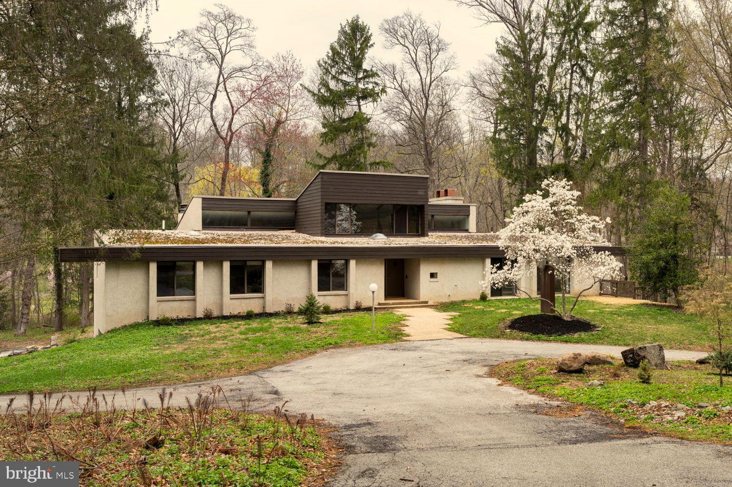 Architect Irwin Stein designed this remarkable home for his own family, bringing his distinctive modernist sensibility to one of the most desirable neighborhoods in Radnor Township. Set on 2.65 acres of secluded, wooded land, the property reflects Stein’s architectural philosophy, where clarity of form, livability, and a connection to the natural environment come together with intention and artistry.
This five-bedroom, five-bathroom residence offers a thoughtful interpretation of modern design. Influenced by midcentury ideals and shaped by the evolving architecture of the late twentieth century, the house blends strong geometry with open, livable space. Its low horizontal profile and expansive glass walls give it a presence that feels both grounded and airy. Carefully planned interiors create a sense of ease and flow from one room to the next.
Signature details showcase Stein’s creativity and craftsmanship. A dramatic spiral staircase, crafted in wood, leads to a serene loft space that floats above the main living area. The circular kitchen is both playful and functional, with original details that reflect Stein’s eye for form. The expansive living room anchors the home with bold architectural gestures—a sunken conversation pit with its own fireplace, a custom built-in sofa, soaring ceilings, and a modernist corner hearth that adds visual balance and warmth.
Floor-to-ceiling windows and glass sliders create seamless connections to the outdoors, where mature trees and natural landscaping surround the house in privacy. Step outside to find an oversized rear deck and patio—perfect for entertaining or enjoying a quiet moment in nature. Every element was carefully considered to ensure the home would feel as inspiring today as it did when it was built.
The lower level adds tremendous flexibility with a second full kitchen, two additional bathrooms, an office or studio, abundant storage, and an oversized four-car garage—ideal for multigenerational living, guest quarters, or creative workspaces.
Ideally situated just minutes from the center of Bryn Mawr, the Stein House offers convenient access to restaurants, shopping, Bryn Mawr Hospital, and the Amtrak station, with easy access to regional rail and major routes. It sits within the award-winning Radnor Township School District and is near some of the region’s most prestigious private schools and country clubs.
Rarely does a property of such architectural integrity and provenance come to market—especially one so ideally located and livable. Designed by Irwin Stein at the height of his creative powers, and cherished by the family who inspired it, 390 S Bryn Mawr Avenue is a one-of-a-kind home that invites you to live with intention, surrounded by beauty.