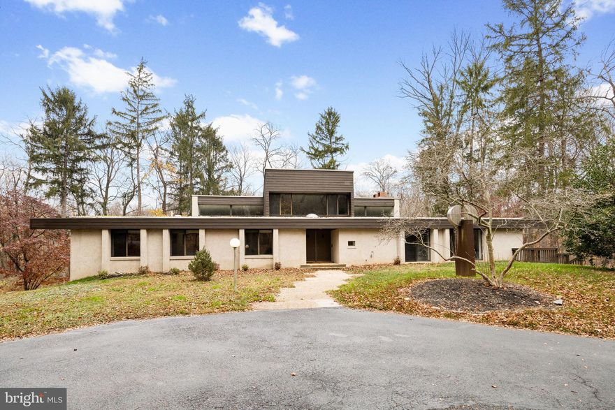 Architect Irwin Stein designed this remarkable home for his own family, bringing his distinctive modernist sensibility to one of the most desirable neighborhoods in Radnor Township. Set on 2.65 acres of secluded, wooded land, the property reflects Stein’s architectural philosophy, where clarity of form, livability, and a connection to the natural environment come together with intention and artistry.

This five-bedroom, five-bathroom residence offers a thoughtful interpretation of modern design. Influenced by midcentury ideals and shaped by the evolving architecture of the late twentieth century, the house blends strong geometry with open, livable space. Its low horizontal profile and expansive glass walls give it a presence that feels both grounded and airy. Carefully planned interiors create a sense of ease and flow from one room to the next.

Signature details showcase Stein’s creativity and craftsmanship. A dramatic spiral staircase, crafted in wood, leads to a serene loft space that floats above the main living area. The circular kitchen is both playful and functional, with original details that reflect Stein’s eye for form. The expansive living room anchors the home with bold architectural gestures—a sunken conversation pit with its own fireplace, a custom built-in sofa, soaring ceilings, and a modernist corner hearth that adds visual balance and warmth.

Floor-to-ceiling windows and glass sliders create seamless connections to the outdoors, where mature trees and natural landscaping surround the house in privacy. Step outside to find an oversized rear deck and patio—perfect for entertaining or enjoying a quiet moment in nature. Every element was carefully considered to ensure the home would feel as inspiring today as it did when it was built.

The lower level adds tremendous flexibility with a second full kitchen, two additional bathrooms, an office or studio, abundant storage, and an oversized four-car garage—ideal for multigenerational living, guest quarters, or creative workspaces.

Ideally situated just minutes from the center of Bryn Mawr, the Stein House offers convenient access to restaurants, shopping, Bryn Mawr Hospital, and the Amtrak station, with easy access to regional rail and major routes. It sits within the award-winning Radnor Township School District and is near some of the region’s most prestigious private schools and country clubs.

Rarely does a property of such architectural integrity and provenance come to market—especially one so ideally located and livable. Designed by Irwin Stein at the height of his creative powers, and cherished by the family who inspired it, 390 S Bryn Mawr Avenue is a one-of-a-kind home that invites you to live with intention, surrounded by beauty.