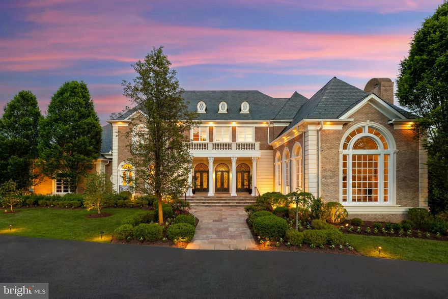 Hidden behind majestic wrought iron gates along a legendary stretch of Potomac’s Millionaire’s Mile is 9421 Newbridge Drive, a neoclassical estate home constructed by master builder David Niroo and crafted by world-renowned designer Haleh Niroo of Haleh Designs. Approached by an elegant crescent-shaped drive, the estate represents a bygone era of fortress-like construction, meticulous workmanship, and an intertwining unparalleled quality with state-of-the-art technology. A triple set of glass and wrought iron entry doors reveal a palatial barrel-ceilinged reception vestibule, opulently lined with inlaid marble floors and Corinthian columns. To one end, a whimsical marble bifurcated staircase, bathed in light from the arched landing window and lined with intricate wrought iron railings, graciously winds itself to the upper level. As with all Niroo mansions, the floor plan is a masterclass in blending grandiose formal rooms with intimate informal areas. Twelve-foot ceilings throughout the main level impart an ethereal flow through the voluminous spaces. The grand salon, a showstopper with its double-height ceiling, soaring Palladian window, and a triple set of French doors, evokes sensations of lavish entertaining during the Gilded Age. The living room features a roaring fireplace, coffered ceiling, and terrace access, yet manages to remain usable despite its formidable scale and luxurious appointments. The dining room features exquisite moldings, a double set of French doors, and effortless flow to facilitate gatherings. A magnificent paneled library with a fireplace and bay window overlooking the grounds offers a post-dinner retreat. The country kitchen is a chef’s dream with furniture-grade inset cabinetry and commercial-grade redundant appliances. The adjacent breakfast room is inviting with its fireplace and terrace access. A comprehensive butler’s pantry and mudroom accessing the four-car garage complete the main level. Sharing an upper-level landing with the grand staircase is the private elevator. Six bedrooms, including a lavish primary suite, feature comforts such as dressing rooms and designer bathrooms befitting those of the world’s most sumptuous five-star hotel rooms. The fully finished lower level is amenity-rich with a large recreation room, wet bar, and private cinema. Sitting above ground and consequently flooded with natural light, the space walks out to a cozy loggia. An additional bedroom suite offers multigenerational flexibility to the highest degree. Out back, the stone terrace looks out to unbroken, verdant vistas and 2.25 acres of level, usable space. Commercial-grade systems are discreetly hidden behind the scenes to ensure peace of mind, as are luxuries such as full audiovisual capability via a video surveillance system and whole-home audio. Unrivaled in workmanship and situated in a prime Falconhurst location, 9421 Newbridge Drive is undoubtedly one of the Capital Region’s great estates.