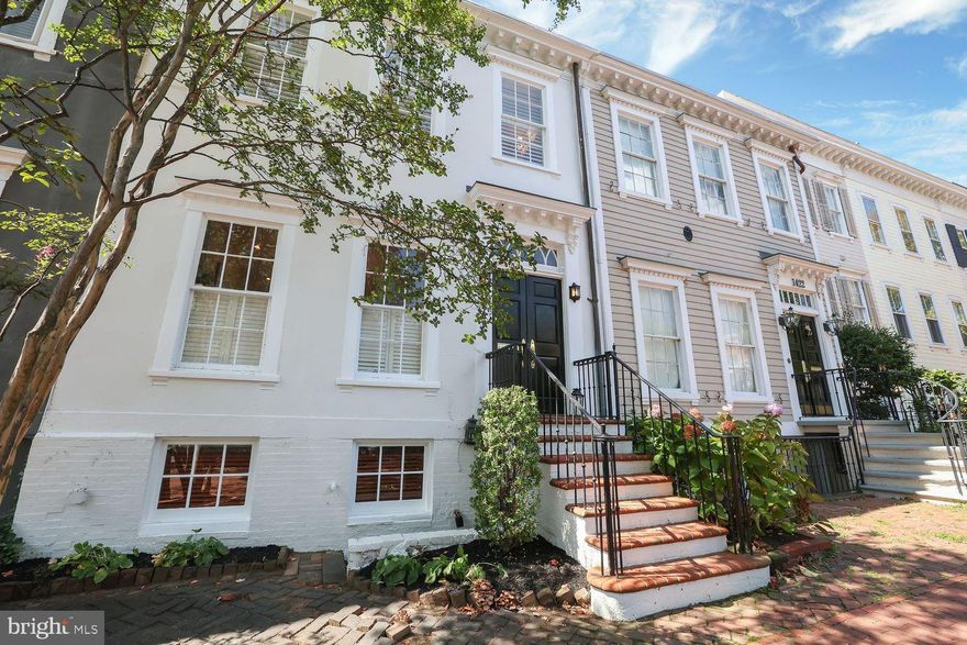 Welcome to 1420 35th Street NW, an elegant Georgetown residence where timeless character and thoughtful updates come together in perfect harmony. Tucked along one of the neighborhood’s most coveted blocks, this classic brick townhome captures the essence of Georgetown living, offering a lifestyle defined by charm, convenience, and sophistication. Just a few blocks from Georgetown University and moments from the vibrant energy of M Street and Wisconsin Avenue, every amenity is within reach, from world-class boutiques and design showrooms to inviting cafés and fine dining. Leisurely strolls along the C&O Canal or afternoons at Georgetown Waterfront Park unfold against a backdrop of cobblestone streets, mature trees, and the historic architecture that has made this community so beloved.

Inside, the home is a study in understated elegance. Custom crown moulding lends refinement throughout, while newly sanded pine floors bring warmth and character to the main level. The formal dining room opens directly onto a walk-out deck overlooking a generous backyard, creating a seamless connection between indoor living and outdoor entertaining. The living room, anchored by a handsome wood-burning fireplace—one of two in the home—sets the tone for gatherings both lively and intimate. Upstairs, two sun-filled bedrooms, each with its own en-suite bath, provide the rare luxury of dual primary suites. Bathed in natural light and framed by charming views, these spaces offer peaceful retreats above the city.

The lower level unfolds as a fully independent guest suite, complete with its own private entrance, full bathroom, and wet bar area. Whether envisioned as an inviting space for overnight guests, a private office, or comfortable quarters for extended family, this level adds a dimension of versatility that elevates the home even further. Beyond the interiors, a private alley leads to two dedicated parking spaces—an invaluable luxury in the heart of Georgetown.

1420 35th Street NW is more than a home; it is a story of refined living in a neighborhood steeped in history and culture. With architectural elegance, rare outdoor spaces, and an unparalleled location, this residence offers a lifestyle as timeless as Georgetown itself.