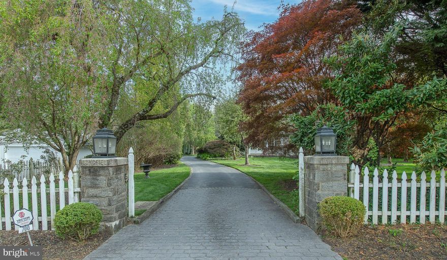Elegant Longfield stone estate nestled on beautifully maintained 1.43 acres with a swimming pool in sought-after Merion Station. This exceptional 6-bedroom, 4 full and 1 half bath residence offers 5,720 square feet of timeless elegance, highlighted by beautiful hardwood floors, intricate crown molding, and classic architectural details throughout.  A gracious formal entry welcomes you into the bright, airy living room with a gas fireplace, which flows seamlessly into a spacious sunroom with its own gas fireplace, perfect for relaxing or entertaining year-round. The formal dining room is richly appointed with crown molding, wainscoting, and a gas fireplace, creating an elegant setting for memorable gatherings, both grand and intimate. French doors lead to a magnificent veranda and a butler’s pantry, offering effortless indoor-outdoor entertaining. The gourmet kitchen is designed for both function and style, featuring a large island with seating, a 6-burner gas cooktop, stainless steel appliances, and a sun-filled breakfast area with a charming bay window and built-in bench. A convenient half bath completes this level. Upstairs, the luxurious primary suite is a private retreat, featuring mirrored French doors that lead to abundant closet space and a spa-like ensuite bath with dual marble vanities, a jetted soaking tub, and a separate shower. Just off the suite is a refined library or office with custom wood built-ins and a gas fireplace. Two additional bedrooms and a full hall bath complete this level. The third floor offers incredible flexibility with a large bedroom or bonus space featuring built-ins, a vaulted beamed ceiling, and a cedar closet, along with two additional bedrooms and two full baths. The lower level offers a 1,000+-bottle wine storage area, a gym or recreation space, laundry, and ample storage. Outside, the magnificent grounds provide both privacy and a stunning backdrop for entertaining, recreation, or relaxation, highlighted by a massive stone terrace, beautiful in-ground pool, lush gardens, and expansive lawn ideal for entertaining. A detached 2-car garage with additional storage completes the property. Ideally located within the top-rated Lower Merion School District, this home is just a short walk to the elementary school and regional rail, and minutes to the shops and restaurants of Narberth and Wynnewood, with easy access to Center City. This exceptional Merion Station estate combines classic elegance, space, and an unbeatable location.