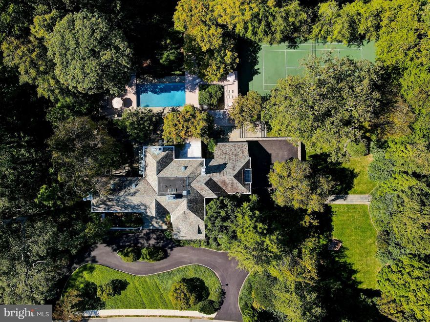 Nestled on one of Baltimore’s finest residential streets,  21 Blythewood Road once served as the residence of Howard Head, a visionary in the sports of tennis and skiing, who invented the oversized tennis racquet and laminated metal skis. Head meticulously redesigned the five-bedroom luxury home and grounds with wonderful living and recreational spaces. Located on nearly two acres in the highly desirable Blythewood community, this English country style five bedroom home welcomes guests into a garden courtyard accented by an antique lamppost. The beaded oak entry door opens into a classic vestibule and foyer. A wide cased portal leads into the adjoining living room featuring an oversized fireplace, concealed bar, built-ins, French doors to the front garden and a breathtaking window wall with sliding doors to the two-tier, 11,000 gallon Koi pond and bluestone patio. Steps from the foyer lead to the solarium with two walls of glass and greenhouse ceiling as well as a wide stone planter open to the adjacent dining room with a fireplace and doors to the patio. The tremendous, Trish Houck designed custom gourmet kitchen provides extensive cabinetry, quartz and granite counters, professional grade stainless appliances and an attached breakfast area, perfect to daydream over coffee through two full-length windows at the patio and pond. A hall leads to the chestnut library with built-in bookcases and cabinetry as well as floor length triple casement windows and a fireplace. A powder room and an exquisite family room with vaulted, wood paneled ceiling, built-ins, wet bar and billiard area complete the main level. A large hall on the second floor flows to a seating area with a fireplace and banister overlook. A private hall provides entry to the primary bedroom suite where a window wall with sliding doors opens onto a large balcony overlooking the Koi pond, pool and extensive woodland garden. Pocket doors lead into the attached dressing room with extensive custom fitted wardrobe cabinetry and a triple casement window and into the primary bath with heated porcelain tile floor, full-width cantilevered double vanity and glass-enclosed shower stall. Two additional, large en-suite bedrooms (one with fireplace) and a bedroom passage leads to bedrooms four and five as well as a hall bath. The third level provides a walk-in cedar closet and additional storage. A back foyer on the lower level leads to the attached three-car garage while a separate hall opens to the laundry room, climate-controlled wine room, exercise room and bath. In addition to the extraordinary back patio and Koi pond, extensive decking and patios lead to the picturesque pool complex with a hot tub, built-in bench seating, and a large custom built-in teak bar. The pool area overlooks the fabled tennis court, specifically designed below grade to ensure a natural barrier to wind. This competition quality tennis complex is one of the most beautiful private courts in the country. Terraced lawns accented by extensive stone garden walls lead to the wooded hillside garden area with floating curved steps, a man-made stream and waterfalls creating a fairytale setting. Designed throughout with state-of-the-art lighting and irrigation and stormwater management systems to maintain this lush venue and showcase it to the best advantage. Located on nearly two gorgeous and thoughtfully landscaped acres, this is a rare opportunity to acquire one of the most spectacular properties in Baltimore.