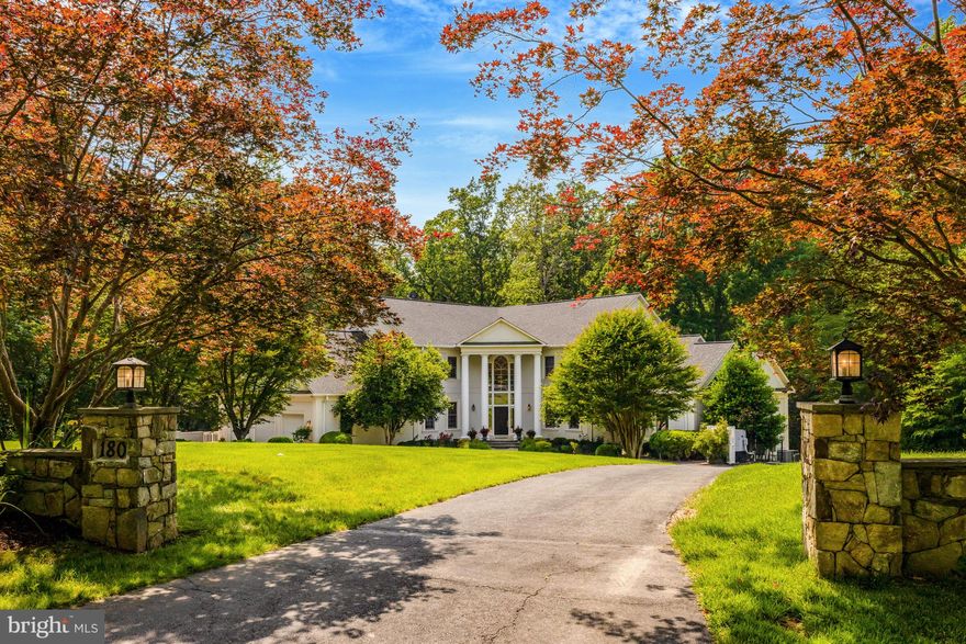 Welcome to this unique V-shaped residence, framed by four stately columns and a soaring artistic Palladian window. This distinguished home, offering 9 bedrooms and 8 ½ baths and providing over 9,000 sq ft of living space, is located in one of the most desired and lovely neighborhoods on the east side of Great Falls; the proximity to the village center, Riverbend Country Club, and the national and regional parks can’t be beat.
An elegant octagonal foyer sets the tone for the home’s refined and thoughtful design. The main level features beautifully refinished hardwood floors and flows seamlessly into a remodeled gourmet kitchen and a dramatic two-story family room, which is framed above by a striking gallery-style promenade. Expansive picture windows throughout flood the home with natural light and offer sweeping views of the surrounding woodlands. The main level also hosts the spacious owner’s suite—a true retreat—featuring a recently renovated bathroom with luxurious, spa-quality finishes.
Upstairs, you’ll find four generously sized ensuite bedrooms, each offering comfort and privacy. The fully finished lower level adds even more versatility, with four additional bedrooms, a full kitchen, and ample space for guests, multi-generational living, or extended entertaining. Outdoors, a private path winds through the backyard, providing direct access to the scenic Potomac River—a rare and coveted amenity.