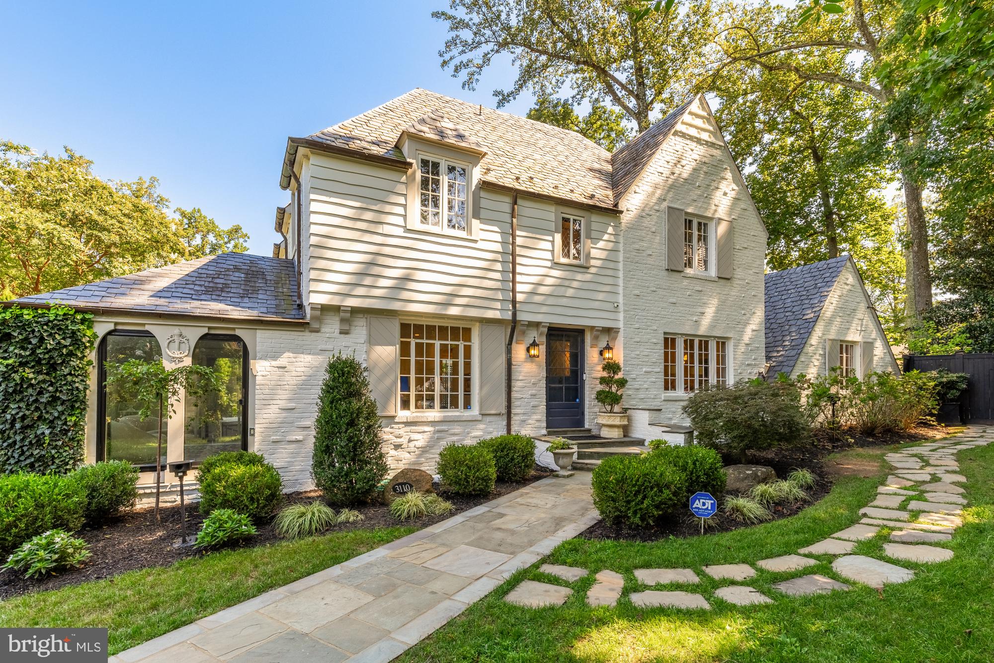Stunning French Normandy Tudor with 5 bedrooms and 4.5 bathrooms, designed by the renowned architect Waverly Taylor. This home features an attached, renovated two-story guest suite, perfect for hosting guests, accommodating extended family, or serving as a private office space. The guest suite's main floor includes a living room, a renovated full bath, and a well-appointed kitchenette equipped with a sink, refrigerator and dishwasher. The upstairs has a bedroom boasting soaring beamed ceilings, recessed lighting, rich wood flooring, and custom railings. This guest suite has multiple glass doors that open onto a spacious patio, perfect for entertaining. This 1935 architectural gem sits on one of Rollingwood's most scenic streets, showcasing a steep slate roof, copper gutters, intricate brickwork, and vintage iron garden gates on a spacious 8,167 sq ft lot.
The main house updates feature a new open-concept gourmet kitchen with white shaker-style cabinets, stunning black marble-look quartzite countertops, and high-end stainless steel appliances, including a Wolf gas stove and Sub- Zero refrigerator, with newly refinished hardwood floors throughout. The spacious living room offers gorgeous, newly refinished hardwood floors, high ceilings, wall-to-wall box molding, and a wood-burning fireplace with an original built-in "ash pit" feature for easy clean-up. The living room opens into a sunroom with a dramatic peaked ceiling that has sliding glass doors to a private travertine patio with a water feature, surrounded by mature landscaping.
The top floor boasts an owner’s suite complete with a walk-in closet and en-suite bath, along with two additional bedrooms and a hall full bath. This level also includes a new stacked washer/dryer. The expansive attic offers ample storage space or room for expansion. On the lower level, you'll find a family room with high ceilings featuring hardwood floors, a fireplace, recessed lighting, along with a fourth bedroom, a full bath, and a bonus workout space.