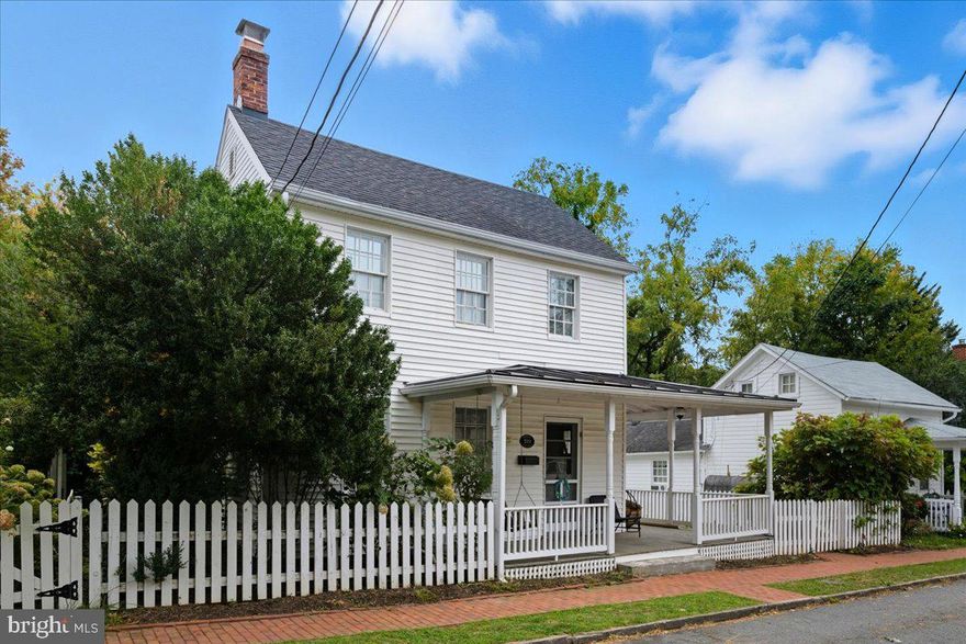 Just beyond Leesburg’s lively King Street, you’ll find a historic home with a garden spirit; where porches invite, perennials bloom, and everyday life feels like a retreat. Set on a quiet residential street, this timeless treasure sits just a block from downtown’s boutiques and restaurants, and nearly next door to the ever-charming Ida Lee Park. Stroll to First Friday festivities filled with music, art, and dining, or wander home to your private oasis, where lush landscaping, a storybook shed, and a broad composite deck promise peace and enchantment in equal measure.

The exterior of this home feels like a page from a garden storybook. The .17-acre lot bursts with stunning landscaping that unfolds like an English garden, thoughtfully planted so that from February through September new blossoms appear in colorful succession. It’s truly breathtaking, and the original landscape design plans will convey to the next owner; a treasure for anyone who delights in nature’s artistry. Beyond the flowers, raised vegetable gardens invite yard-to-table meals, while a graceful fence and arbor frame the space with charm. An underground irrigation system keeps everything thriving with ease.

The backyard is anchored by a spacious deck and paver patio, perfect for entertaining or simply soaking in the view of your private sanctuary. Just beyond, a large shed with metal roofing and full electricity feels almost like a whimsical cottage, ready to serve as a workshop, studio, or secret hideaway. Together, these spaces create an outdoor retreat as practical as it is enchanting.

Inside, over 2,000 finished square feet wrap you in warmth and character. Original hardwood floors, two working fireplaces, and both front and rear staircases whisper stories of the past, while modern updates make life easy. 

The kitchen, fully renovated and gleaming with crisp white cabinetry, granite counters, and stainless appliances, makes staying in as delightful as dining out. It opens to a sunny dining nook, a cozy spot for morning coffee overlooking the yard. A formal dining room, anchored by its own fireplace and the original rear staircase, serves as a warm gathering space. The living room, with its second fireplace, connects seamlessly; a welcoming space for conversation, comfort and togetherness.

The main-level primary suite, renovated in 2018, is a retreat all its own with a private porch entrance. Its spa-like bath features river rock tile, updated fixtures, and modern finishes throughout. A separate laundry room with a newer pedestal washer and dryer completes the main level.

Upstairs, two generous bedrooms with plenty of closet space and breezy ceiling fans offer restful retreats. A full bath and an airy landing add both function and charm.

Behind the beauty, this home is just as sound. Dual-zone HVAC, a newer hot water heater, public utilities, and high-speed internet ensure modern convenience.   This home is more than walls and windows; it’s a charming slice of life in Historic Downtown Leesburg. Here, small-town character blends with endless activities to create a lifestyle that feels both lively and peaceful, timeless yet refreshed, and every bit as magical as it is real.