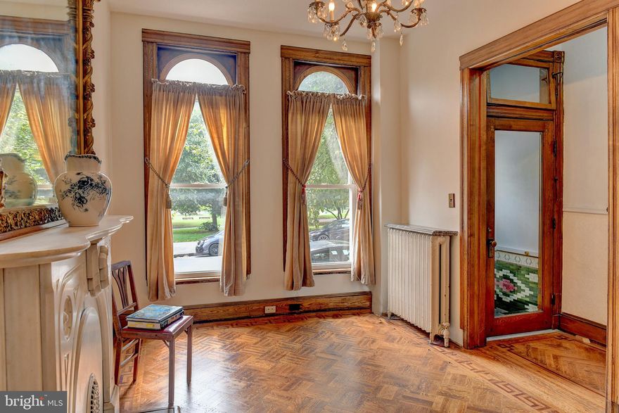 In a city crowded with countless row houses on narrow streets, you’ll appreciate this generous residence. Welcome to 2744 E Baltimore Street, an iconic home overlooking Patterson Park, where historic charm and city living come together in a way that’s increasingly hard to find.

As you enter under the bejeweled stained glass arch bearing the home’s address and step into a beautifully tiled foyer, you immediately know you’ve found something special.

The sitting room to your right showcases a stunning 5-foot Rococo gilt mirror set above a white marble fireplace—an elegant nod to the home’s turn-of-the-century origins. Hidden within the walls are beautiful oak pocket doors, and throughout, each room features its own unique hardwood floor design. Soaring ceilings and oversized proportions create a sense of space and grandeur.

Continue into the spacious dining room, where a gleaming tin ceiling makes a striking impression. This space flows seamlessly into a renovated Craftsman-style kitchen featuring milk glass inserts and the original 1919 tin ceiling—blending thoughtful updates with timeless character.

Just off the kitchen, the mudroom offers convenient laundry and access to a full bath, adding everyday functionality to the home’s historic charm.

Step outside to your private patio—perfect for summer barbecues, quiet mornings, or evening gatherings.

The second level continues the home’s historic narrative with a spacious front bedroom overlooking Patterson Park, offering ever changing, spectacular seasonal views. Two additional bedrooms—each with their own character—feature charming chandeliers, with one showcasing exposed brick for a warm, textured feel. The original bathroom is a true showpiece, complete with an oversized clawfoot soaking tub, classic tile flooring, a marble vanity, and a chandelier that evokes the elegance of the Gilded Age—a space that feels both timeless and indulgent.

The third floor offers incredible flexibility, featuring another large front bedroom with sweeping park views, along with a kitchenette and full bath—ideal for guests, extended living, extra income, or a private retreat.

Enjoy elevated city and rooftop views right from your kitchen table or even while unwinding in the bath.

This home is ready for its next chapter—an opportunity to customize and make it your own while preserving its rich character. Lovingly maintained and improved by the current owner over the past 31 years, key updates include a new boiler (2022), water heater (2023), washer and dryer (2023), windows (2022), and a remodeled kitchen (2020). Major system upgrades were completed in 2005, including plumbing and electrical, along with a roof replacement in 2014.

Park-front living isn’t just a location—it’s a lifestyle. Just outside your door, Patterson Park offers scenic walking and running trails, open green space, a lake, playgrounds, tennis and basketball courts, a dog park, community events, and iconic city views from the Pagoda. Ideally located just minutes from the waterfront, Canton, Fells Point, Johns Hopkins, and major commuter routes including I-95, I-895, and I-83, this home delivers both charm and convenience. Recently rented for $2,500.