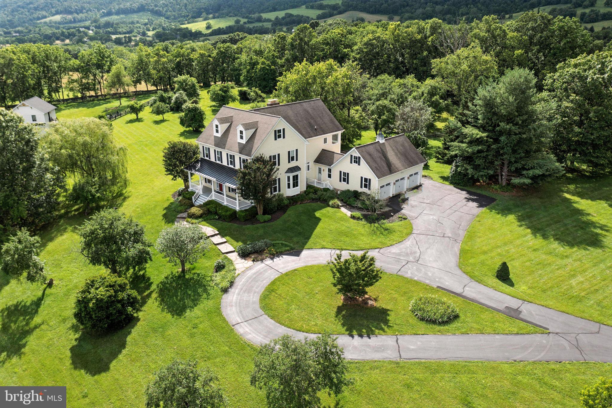 Private Estate with Sweeping Blue Ridge Mountain Views | Over 6,600 Sq Ft on Nearly 4 Acres
Tucked at the end of a quiet cul-de-sac in Round Hill, Virginia, this custom-built estate offers the perfect blend of privacy, space, and panoramic mountain views. With over 6,600 square feet of finished living space on 3.77 scenic acres, this home is a rare find for those seeking beauty both inside and out.
A charming oversized front porch welcomes you home with serene views of rolling hills, mature landscaping, and the stunning Blue Ridge Mountains. Inside, rich hardwood floors and abundant natural light create a warm and inviting atmosphere throughout. The main level features a sun-drenched family room with a fireplace, a formal living room, a formal dining room, a private office, and a spacious kitchen outfitted with granite countertops, stainless steel appliances, a center island, and an oversized butler’s pantry—perfect for everyday living and entertaining alike. With 5 bedrooms and 4.5 bathrooms, there’s plenty of room for everyone. The expansive primary suite offers a private retreat with its own fireplace, spa-like bath with dual vanities, a soaking tub, and a huge walk-in closet. Additional bedrooms are generously sized and beautifully appointed. The finished third-level attic is full of charm and flexibility—complete with a private bedroom, unique architectural angles, and cozy nooks, it’s perfect for a teen suite, creative workspace, guest hideaway, or quiet reading retreat. Above the 3-car garage, a finished bonus room makes an ideal art studio, workshop, hobby space, or home office. The fully finished basement expands your options even further, offering space for recreation, multi-generational living, or additional entertaining. Step outside and enjoy peaceful outdoor living from the covered porch or the expansive stone patio—perfect for relaxing mornings, summer gatherings, or evenings under the stars with the mountains in view. With its quiet location, spacious layout, and unbeatable views, this move-in ready estate is a true gem. Schedule your private tour today!