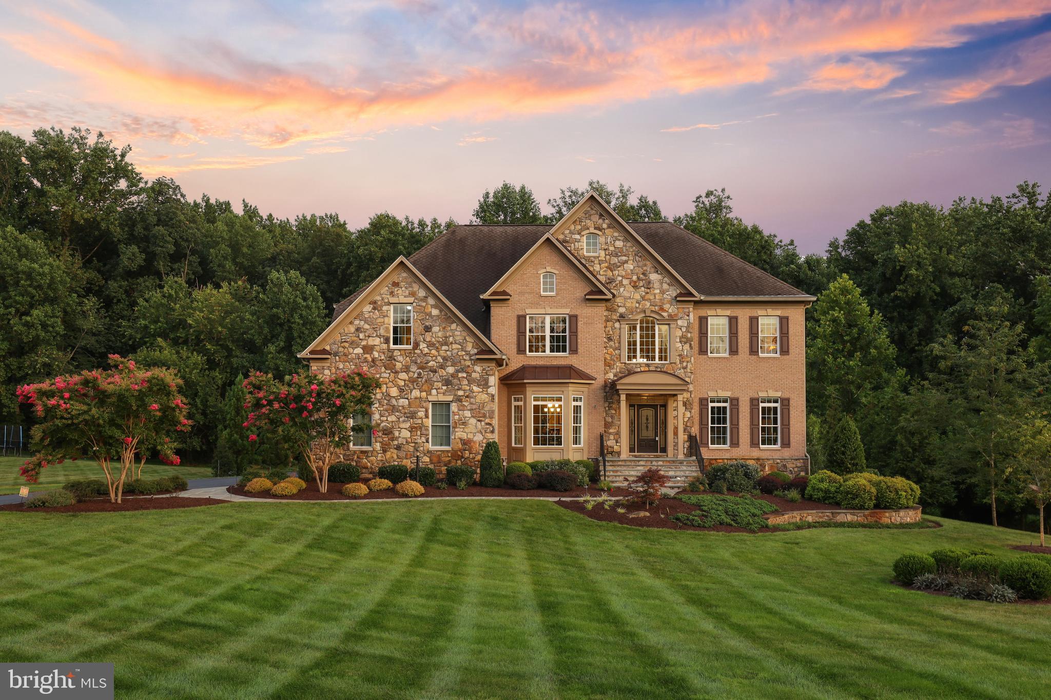 Set on a private 1.15 acre homesite in coveted Riverwood, this stone accented colonial offers over 8,960 finished square feet, luxurious features, and a backyard oasis. A grand two-story foyer ushers you inside to find enriched Brazilian cherry hardwoods, tray ceilings, exquisite trim, a formal living room with heightened windows and a deep tray ceiling, a formal dining room with a brilliant bay window, a butler’s pantry with a beverage fridge, and a private study complete with French doors, stacked cherry moldings, a bay window, and custom built-ins. Captivating two-story family room features a floor-to-ceiling stone fireplace, deck access, and an ideal flow into the gourmet kitchen followed by a defining sunroom with transom topped windows, a tray ceiling, a designer leaf fan, and a walkout to the deck with spectacular private thick tree-lined views. Richly appointed, the kitchen is equipped with 42" crown cherry cabinetry, sleek granite counters, complementing tile backsplash, a walk-in pantry, an oversized center island with a breakfast bar, a deluxe line of stainless appliances including a 7-burner gas range, a wine cellar, a custom range hood, and an open breakfast room. Upstairs is designed with three secondary bedrooms each with spacious walk-in closets and completed by an expansive owner's suite presenting a tray ceiling, a large sitting room, three walk-in closets, and a deluxe bath showing dual vanities, an oversized multi-head shower, a huge warming area, and a platform soaking tub. Rich with design elements, the lower level haven displays engineered hardwoods, a rec room enhanced by an ambient gas fireplace, a robust wet bar, a game room with a walkout to a covered patio studded with columns and twin fans, a theater and golf room, a home gym with rubber flooring, a bedroom, a full bath, extra storage, and a bonus room. Providing an outdoor entertainment venue and where you can enjoy relaxing evenings watching the sunset is a Fiberon low maintenance deck, a lower bluestone patio with an outdoor kitchen, a fire pit, outdoor audio and video, a Strong Spa hot tub, custom lighting, and a firepit with custom seating. Experience this plush hallmark home in a notable Howard County location with beautiful surroundings.