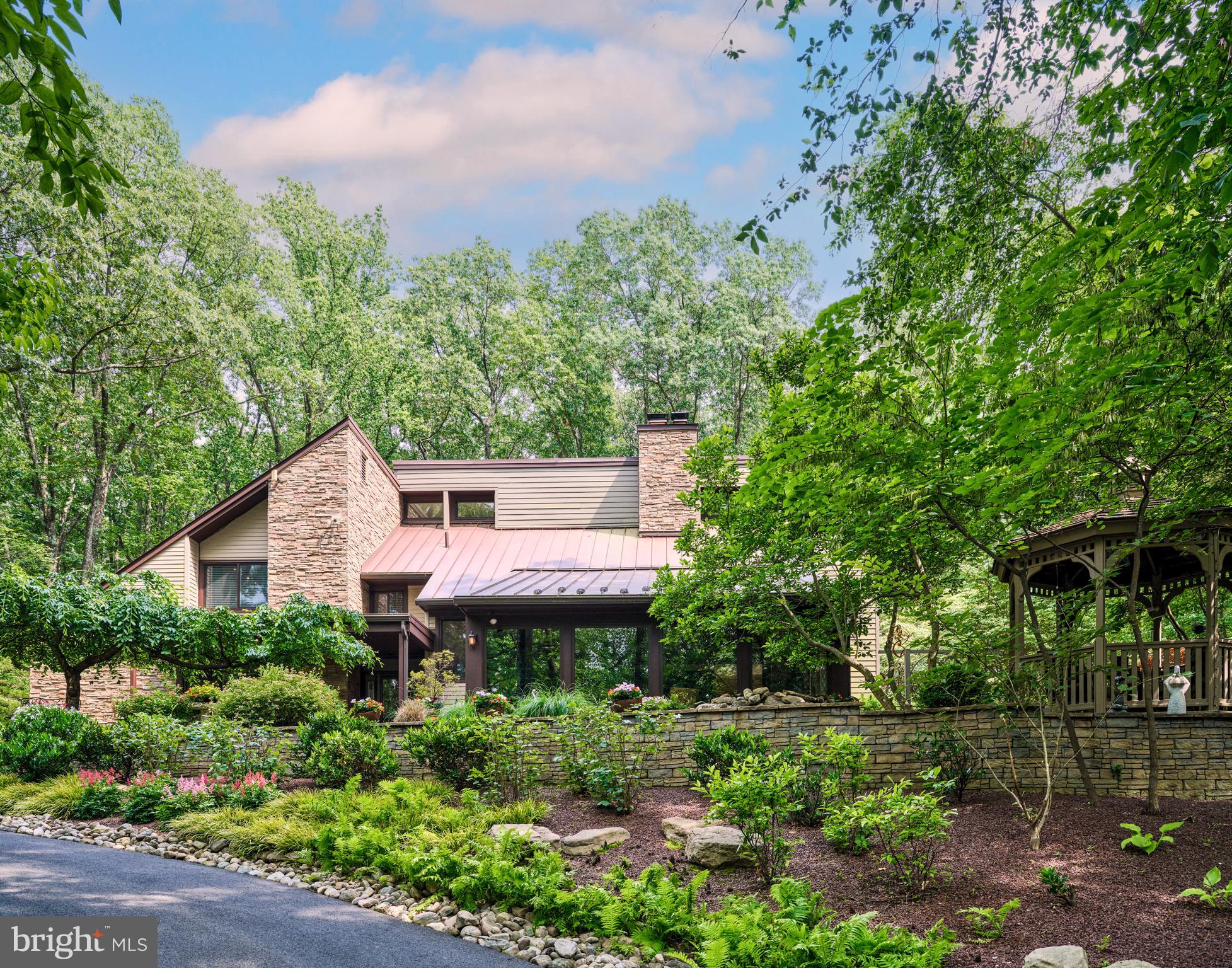 Embrace the joy of discovering "Paradise Found," a contemporary oasis nestled amidst nearly five private acres of enchantment, serenity, and natural splendor. A meandering driveway, bordered by stone terraces, mature gardens, meditation trails, and a richly populated koi pond, leads you to the hidden jewel of Ely Road in the charming town of New Hope, Pennsylvania. As you step inside, the main floor offers a well-lit office space and an awe-inspiring two-story great room, featuring mirroring custom built book shelves that stretch from floor to ceiling. Adding a touch of rustic charm is a stone-finished wood-burning fireplace and a grand window display, allowing you to soak in the beauty of the gardens that encapsulate the property. The kitchen, both welcoming and functional, boasts a central island complete with a cooktop, a wall oven & warming drawer, a custom-made workstation, and a glass-walled sunroom offering stunning views of the pool haven. The journey upstairs brings you to the sumptuous primary suite, complete with a secluded deck off the bedroom, a luxurious bathroom w/ double vanity and glass shower, and a large walk-in closet with a private deck of its own. The second level also offers two additional, generously sized bedrooms, each adorned with skylights and equipped with their own bathrooms for ultimate convenience. Adding to the exclusivity of the property is a custom-built wine cellar, showcasing an impressive wall of wine bottles and a full bar. The backyard is a spectacle of its own with lush flowers and stone walls encircling the heated, saltwater pool with a cascading hot tub. Spend warm summer evenings around the outdoor fire pit, basking in the glow of an outdoor oasis illuminated by extensive landscape lighting. A freestanding garage, roomy enough for three cars, offers additional parking while providing a pristine work area for your tools and toys. This impeccably kept retreat is situated minutes away from the center of town, nestled within the prestigious New Hope-Solebury School District, and is strategically positioned nearby all primary commuter routes. If you've been on a quest for your next chapter, the one unique story that not only resonates with your head but also with your heart, then you have arrived at "Paradise Found". (Sellers are including ALL furniture and contents within home, both interior and exterior, with the sale.)