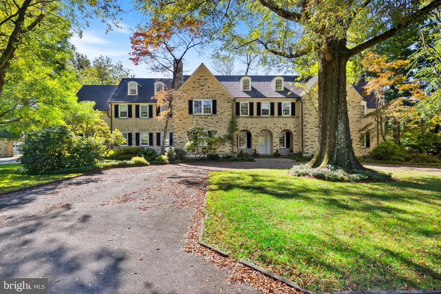 If you appreciate excellence, you will understand what makes this property so special. From its inlaid wood, tile and slate flooring and intricate moldings to its 10-foot ceilings and Ludowici terracotta tile roof, with details like a wrought-iron grille over the coat closet window to call bells to summon the staff, this 1911 Tudor Revival Normandy-style home is a masterpiece of craftsmanship. Built of Wissahickon schist, the main 9,024- square-foot, 3-story stone main house features 8 bedrooms, 6 full and 2 half baths, and 6 wood-burning fireplaces. Originally designed by noted Philadelphia architect Charles Barton Keen, it was updated in the 1930s by architect Sydney Martin, has been renovated multiple times since and was just painted throughout. A detached garage with 5 bays includes a 2-bedroom, 2-bath apartment with kitchen and family room. Protected by a conservation easement, this stunning 3.6-acre garden oasis boasts specimen trees and an enviable location across from Carpenter’s Woods, Philadelphia’s first bird sanctuary, and abutting the Wissahickon Valley Park, with miles of trails for hiking, biking and horseback riding. In one of the most architecturally and naturally stunning neighborhoods of Philadelphia, the property offers easy access to Chestnut Hill, Center City and beyond. 
Off the circular driveway, follow the slate walkway through graceful arches to the front door and the grand entrance foyer beyond. In front of you, the sun room offers gorgeous views of the terrace and rear yard through 3 sets of French doors. Its slate floor coordinates with the colors of the elegant hand-painted Gracie wallpaper in the living room to its right and the dining room to its left. Both are accessible through beautiful sliding pocket doors from the sun room or through double doors from the foyer. The living room features a fireplace with a recently paneled surround. It also opens to the terrace through French doors. An archway leads to a sunlit music room with thick moldings and deep window sills. To the right of the foyer is a cozy, wood-paneled office with a fireplace and built-ins. Nearby, a magnificent circular staircase leads to the second level, and a stairwell leads to the lower-level caterers’ kitchen, which opens to an outside patio.  
To the left of the sunroom, bowed glass windows fill the formal dining room with light. It’s a welcoming setting for both formal and informal meals, with a fireplace, intricate moldings, built-in glass cabinets, stunning wallpaper and French doors to the terrace. Just beyond, the bespoke gourmet kitchen was renovated in 2011. It boasts 3 Sub-Zero refrigerators—a refrigerator, a freezer and a wine cooler with refrigerated cabinet drawers—and a Wolf range. Notice the dental moldings and the handsome silver pot rack above the double-thick marble center island with seating for 4. Once used as staff quarters, the wing off the kitchen now houses a breakfast room, informal family room, pantry and powder room. Back staircases lead to the second level, the lower-level and the backyard. 
On the second level, the interconnected rooms off the main hall in the back of the home—dual bedrooms, baths and sitting rooms—could be converted to a large primary suite. French doors open to a balcony over the music room overlooking the backyard. Across the center hall are 2 bedrooms with en suite baths, one recently updated; 2 additional bedrooms that share a full bath in the hall; a homework room and a closet room with built-in cabinets. Stairways at either end of the hall lead to the third level, which has a playroom with built-ins and arched windows, 2 additional bedrooms, a bath, cedar closets and access to the attic.
In-ground pool and Har-Tru tennis court(needs renovation), and it’s the perfect setting to raise your family and entertain guests. The property has parking for 20+ cars and is just 5 minutes from the Chestnut Hill West rail line. 2 miles from the heart of downtown CHil