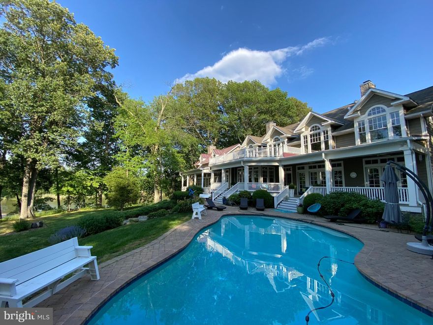 With approximately 2,650 feet of private waterfront along Southeast Creek and sweeping views toward the Chester River, this exceptional 13.2-acre estate in the desirable Kennersley Farm community offers the rare combination of protected water, expansive acreage, and extraordinary privacy — complemented by a beautifully crafted main residence and detached carriage house.
Originally constructed as a builder’s personal residence, this coastal farmhouse showcases exceptional craftsmanship and enduring quality throughout. The main home offers eight bedrooms and six-and-a-half baths, including three private ensuites thoughtfully positioned for comfort and privacy. A detached stone carriage house provides two additional bedrooms, a full kitchen, and bath above a side-loading two-car garage with conditioned workshop and storage space — ideal for extended guests, multigenerational living, or private accommodations.
Inside, timeless architectural details define the interiors: wide hewn pine hardwood flooring, substantial eight-inch base trim, solid wood doors, raised panel wainscoting, and four fireplaces that add warmth and character throughout. The waterside great room serves as a striking focal point, featuring a coffered ceiling, a dramatic stone fireplace with a custom mantel designed by Vicco VonVoss, built-in media cabinetry, and breathtaking water views. A central gourmet kitchen anchors the home and flows seamlessly into expansive gathering spaces, including a remarkable three-sided waterfront game room with pool table that conveys — designed for year-round entertaining.
The main-level ensuite with adjoining sunroom opens to a private side deck, creating an ideal space for quiet mornings or evening retreats. Upstairs, the primary suite offers built-in bookcases, a fireplace, generous walk-in closets, a jetted tub, and plumbing for a future steam shower. An additional expansive ensuite on the second level provides exceptional privacy and includes a separate sitting area large enough for a sofa — perfect for guests seeking their own retreat. Additional bedrooms on the upper level provide ample space to relax and unwind. Dual laundry rooms on both the main and upper levels enhance everyday convenience, while a finished attic suite with sitting area and half bath offers additional flexibility. The unfinished walk-up basement with exterior access presents an opportunity for future customization.
Outdoor living rivals that of a private resort. A waterside saltwater pool with a 10-foot diving well and diving rock is surrounded by an expansive paver patio, while a 12-foot-deep wraparound porch, tiered covered porch, upper balcony, and stone fire pit provide multiple vantage points to enjoy sunset views over the water. Custom exterior lighting enhances the architecture and landscaping in the evening, while a private, alarm-secured driveway ensures a refined sense of arrival and seclusion.
The private dock has electric service run to it and water access, along with two boat slips and two jet ski lifts, providing direct access to Southeast Creek and beyond. A natural shoreline, kayak launch, mature trees, and resident bald eagles enhance the serenity of the setting. Just minutes from Kennersley Point Marina and within easy boating distance to Chestertown, Rock Hall, and Annapolis, this estate offers both tranquility and accessibility. The residence is also being offered fully furnished, presenting a rare turnkey waterfront opportunity.
Defined by the elements that matter most — substantial water frontage, protected deep water, acreage, privacy, quality construction, and turnkey furnishings — this is a legacy offering for refined waterfront living on Maryland’s Eastern Shore.