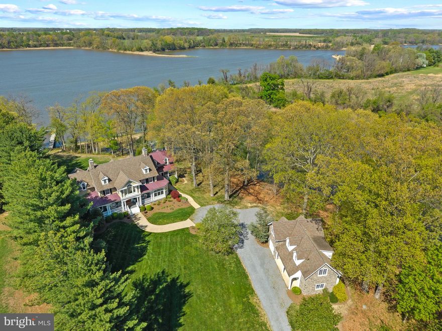 With approximately 2,650 feet of private waterfront along Southeast Creek and sweeping views toward the Chester River, this exceptional 13.2-acre estate in the desirable Kennersley Farm community offers the rare combination of protected water, expansive acreage, and extraordinary privacy — complemented by a beautifully crafted main residence and detached carriage house.
Originally constructed as a builder’s personal residence, this coastal farmhouse showcases exceptional craftsmanship and enduring quality throughout. The main home offers eight bedrooms and six-and-a-half baths, including three private ensuites thoughtfully positioned for comfort and privacy. A detached stone carriage house provides two additional bedrooms, a full kitchen, and bath above a side-loading two-car garage with conditioned workshop and storage space — ideal for extended guests, multigenerational living, or private accommodations.
Inside, timeless architectural details define the interiors: wide hewn pine hardwood flooring, substantial eight-inch base trim, solid wood doors, raised panel wainscoting, and four fireplaces that add warmth and character throughout. The waterside great room serves as a striking focal point, featuring a coffered ceiling, a dramatic stone fireplace with a custom mantel designed by Vicco VonVoss, built-in media cabinetry, and breathtaking water views. A central gourmet kitchen anchors the home and flows seamlessly into expansive gathering spaces, including a remarkable three-sided waterfront game room with pool table that conveys — designed for year-round entertaining.
The main-level ensuite with adjoining sunroom opens to a private side deck, creating an ideal space for quiet mornings or evening retreats. Upstairs, the primary suite offers built-in bookcases, a fireplace, generous walk-in closets, a jetted tub, and plumbing for a future steam shower. An additional expansive ensuite on the second level provides exceptional privacy and includes a separate sitting area large enough for a sofa — perfect for guests seeking their own retreat. Additional bedrooms on the upper level provide ample space to relax and unwind. Dual laundry rooms on both the main and upper levels enhance everyday convenience, while a finished attic suite with sitting area and half bath offers additional flexibility. The unfinished walk-up basement with exterior access presents an opportunity for future customization.
Outdoor living rivals that of a private resort. A waterside saltwater pool with a 10-foot diving well and diving rock is surrounded by an expansive paver patio, while a 12-foot-deep wraparound porch, tiered covered porch, upper balcony, and stone fire pit provide multiple vantage points to enjoy sunset views over the water. Custom exterior lighting enhances the architecture and landscaping in the evening, while a private, alarm-secured driveway ensures a refined sense of arrival and seclusion.
The private dock has electric service run to it and water access, along with two boat slips and two jet ski lifts, providing direct access to Southeast Creek and beyond. A natural shoreline, kayak launch, mature trees, and resident bald eagles enhance the serenity of the setting. Just minutes from Kennersley Point Marina and within easy boating distance to Chestertown, Rock Hall, and Annapolis, this estate offers both tranquility and accessibility. The residence is also being offered fully furnished, presenting a rare turnkey waterfront opportunity.
Defined by the elements that matter most — substantial water frontage, protected deep water, acreage, privacy, quality construction, and turnkey furnishings — this is a legacy offering for refined waterfront living on Maryland’s Eastern Shore.