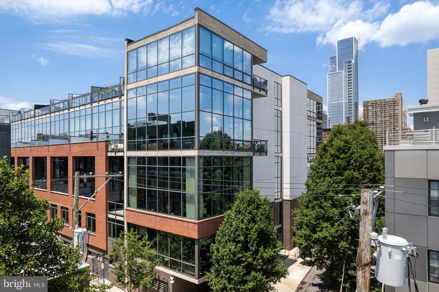 Price Improvement! Seller has prepaid special assessment!
Welcome to Unit 217B at the coveted 1352 Lofts—a rare corner unit that redefines modern loft living with soaring ceilings, wall-to-wall glass, and warm contemporary finishes. This sleek, sun-drenched residence blends bold industrial character with everyday comfort in the heart of Philadelphia’s vibrant Avenue of the Arts district.

An expansive open layout showcases floor-to-ceiling windows wrapping two full walls, bathing the space in natural light and offering lush green views in the warmer months and cityscapes year-round. Rich hardwood floors run throughout the unit, complementing the exposed ductwork, concrete ceilings, and architectural columns that define the loft aesthetic.

The spacious kitchen is designed for both beauty and function, with dark flat-front cabinetry, granite countertops, a striking mosaic tile backsplash, stainless steel appliances, and a generous peninsula with bar seating—perfect for entertaining or casual nights in. The adjacent living and dining areas flow seamlessly together, with ample room for a home office, oversized sectional, or even a studio setup.

Step outside onto your private balcony—a true city oasis. Tucked just above street level and flanked by trees and urban views, it's an ideal spot to relax with your morning coffee or unwind with a cocktail after work.

The large bedroom offers privacy and tranquility with a full en-suite bath and walk-in closet, while an additional full bathroom provides convenience for guests.

This professionally managed, elevator building offers secure keyless entry, sprinkler systems, and a 24-hour front desk concierge. Deeded parking space #59 is included in the sale price.

Just steps from Broad Street, the Broad Street Line, Whole Foods, ACME, Seger Park, and some of the city’s best restaurants, galleries, theaters, and cafés—you’ll be at the crossroads of convenience and culture. Whether you're heading downtown, walking to Rittenhouse, or hopping on public transit, this location puts it all within reach.

Don't miss the chance to call one of Philadelphia’s most architecturally distinctive loft buildings your new home