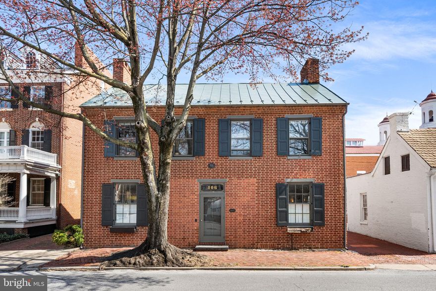 Welcome to 106 N Court St, a timeless 1865 historic home ideally located in the heart of Downtown Frederick, directly across from City Hall. This classic residence blends historic charm with thoughtful updates, including a new AC system in 2025 and efficient boiler heat, all within one of the most walkable and vibrant areas in the city.

The main level showcases hardwood floors throughout, abundant natural light, and undeniable character at every turn. The spacious living room features custom built-ins and a cozy fireplace, creating a warm and inviting space to gather. A formal dining room with its own fireplace offers the perfect setting for entertaining. The updated kitchen is designed for both function and style, featuring an abundance of cabinet space, a center island with a built-in gas range and bar seating, and windows overlooking the private full brick patio. A convenient half bath completes the main level.

Upstairs, hardwood flooring continues throughout. The primary bedroom offers a fireplace and generous closet space, combining comfort with classic charm. A second bedroom features an updated en suite full bath, while an additional bedroom and another full bathroom provide flexibility for guests, work-from-home needs, or additional living space. A full basement offers excellent storage.

Outside, the private full brick patio creates a peaceful retreat rarely found in downtown living, complemented by rare 2-car private off-street parking.

Living here means stepping directly into everything Downtown Frederick has to offer. Enjoy your mornings at Gravel & Grind or Frederick Coffee Co., grab lunch at Firestone’s Culinary Tavern or Café Nola, and spend evenings at local favorites like Brewer’s Alley, Tenth Ward Distilling, or McClintock Distilling. With boutique shopping, art galleries, Carroll Creek, and year-round events just steps away, this location offers an unmatched lifestyle in one of Maryland’s most charming historic downtowns.