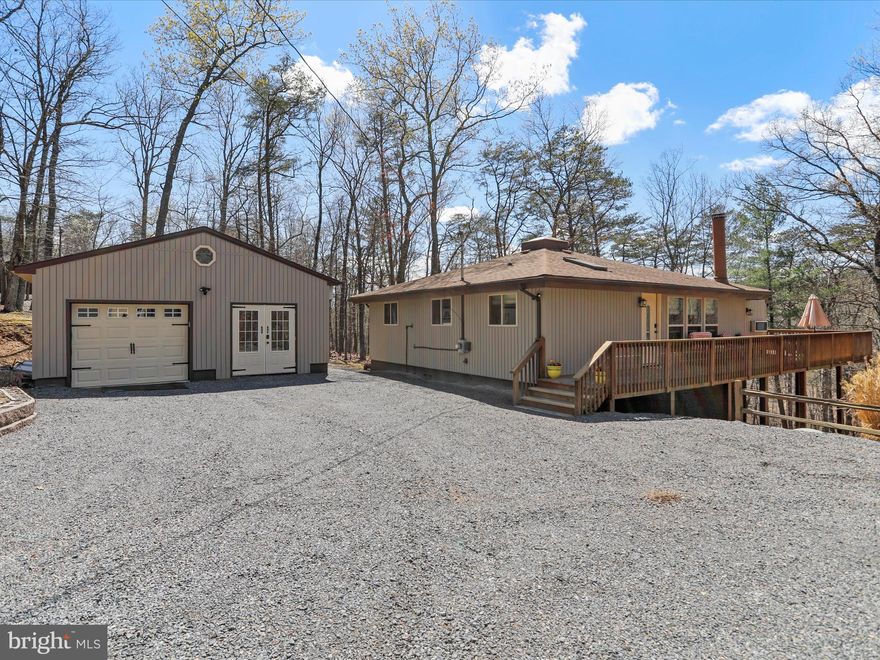 PRICE IMPROVEMENT! Tucked on a wooded lot just under 2 acres, this lovingly maintained home wraps you in comfort the moment you arrive. From the thoughtfully upgraded main house to the beautifully finished studio space in the detached garage, every inch of this property radiates care, quality, and character.
Let's start with the office/studio-accessed via French doors or from the garage. This vaulted, open-beam, tongue-and-groove-ceiling space is finished with industrial-grade vinyl flooring, a decorative ceiling fan, custom built-in desk and cabinetry, laminate counters, and storage hidden behind stunning barn doors. It's climate-controlled with a remote HVAC system and conveys with the TV. Whether you need a home office, craft room, guest retreat, or creative studio, this space adapts with style.
The home's immaculate wraparound deck has been extended for outdoor living, with traditional wood railings reinforced by modern coated wire-an on-trend upgrade that adds both beauty and safety. Enter through the side door into a spacious and serene entry retreat—a beautifully finished room with built-in cabinetry, quality industrial carpet, and vaulted, wood-lined ceilings. Whether you're storing gear, relaxing on the daybed with a good book, or greeting the day with a cup of coffee, this space blends function and soul in all the right ways.
One children's bedroom sits just beyond, sweetly styled with a stained-glass ceiling light and double closets. French doors open to the heart of the home a magnificent great room with soaring vaulted ceilings, exposed beams, skylight, hardwood floors, and a wood-burning corner fireplace. Decorative lighting and a unique ceiling fan round out the charm.
The Chef's Kitchen is a dream. Custom KraftMaid cabinetry, granite counters, glass backsplash, stainless steel appliances, 5-burner ceramic cooktop, corner cabinet carousels, full-size double convection ovens, a deep sink, microwave, pantry, wine bar, and under-cabinet glass holders-all lit with perfectly placed track lights. There are too many thoughtful, high-end features to list-this kitchen truly delivers both style and function.
The adjacent laundry room is a surprise delight: vaulted ceiling, durable vinyl floors, full-size washer and steam dryer, linen closet, and a tucked-away desk nook.
The guest bedroom features a vaulted ceiling, exposed beam, Berber carpet, closet for storage, and a ceiling fan with light.
The serene primary suite easily fits a king-sized bed, with a vaulted ceiling, Berber carpet, and wall-mounted reading sconces. The en-suite bath features a custom-tiled, oversized shower with glass doors and a five-shower-head spa system, plus a glass block window for natural light and privacy.

Additional features include:
 • New vinyl siding (2024) and all new windows (2014)
• Fresh interior paint throughout
• Oversized and illuminated crawlspace with pristine vapor barrier
• Detached one-car garage with vaulted ceiling, built-ins, separate electric, and refrigerator that conveys
• Large garden shed for tools and outdoor gear
• Deck lighting for evening ambiance
• New French drain beside garage
• Lots of parking in the crush-and-run stone driveway
• Consistent preventative maintenance and pest service
• All window treatments convey
• A list of select furniture and items that convey is available upon request

This home also includes a Class A membership to The Woods Club, granting access to championship golf, indoor/outdoor pools, tennis, fitness center, clubhouse, trails, and more.
Simply put: this home feels like a bear hug. It's peaceful, practical, and full of possibility.
And it's ready for its next chapter.