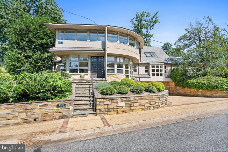 This beautiful contemporary residence is ideally located in the highly desirable Kent neighborhood. Set off the street on a large corner lot, the house captures an abundance of natural sunlight from impressive oversized windows and exposures on all sides. The house was originally designed in 1950 by an architect influenced by Frank Lloyd Wright and has since been renovated and expanded by architect Lloyd Jafvert. Jafvert also transformed the orientation of the residence so that the primary entrance could be from both Loughboro Road and Chain Bridge Road. The house features beautiful architectural details and a wonderful open floor plan, which is perfect for large-scale entertaining. There is an easy flow between the generously-scaled formal rooms on the main level and seamless transition from indoors to outdoors. One of the unique features of this home is the opportunity for MULTIGENERATIONAL LIVING. There is a very attractive private entrance to the left of the front door that opens to a generous suite. The suite offers a large living room with built-ins, a bedroom area, bathroom, kitchenette, and library. The dramatic entry foyer features double wooden doors and a lovely slate floor. It extends a visual invitation to the rear of the home, with sightline views through the gracious center hall and a glimpse of the formal dining room to the right. The sophisticated dining room has a tray ceiling and built-in serving station. It adjoins the formal living room, which offers a beautiful marble fireplace and windows overlooking the grounds. The updated gourmet chef’s kitchen is well-appointed with stainless steel appliances and a dual-sided central island. There is also abundant cabinetry storage, breakfast bar seating, and oversized grid-inspired windows, providing the space with remarkable natural sunlight. The kitchen opens to a breakfast room and then to a family room with an additional fireplace. There is a large bedroom suite and an additional bedroom with an en-suite bathroom completing this floor. The upper level was designed to showcase an exceptionally-scaled primary suite. The bedroom offers a soaring Cathedral ceiling, concealed kitchenette, built-ins, large windows, and exterior access to a private deck. The en-suite bathroom has two sinks, a built-in vanity, walk-in shower, and a separate Jacuzzi soaking tub. The suite also has two-walk-in closets, secondary closets, and a private sitting room. There is an additional bedroom on this floor, which is spacious with its own bathroom. The lower level of the home offers a multitude of flexible spaces, including a large recreation room with a bar and fireplace, a game room, wine room, laundry room, and abundant storage. There is also a garage accessed from this level. The grounds are extensive and offer multiple seating areas for outdoor entertaining. The house is also within close proximity to neighborhood favorite restaurants, shops, and parks.