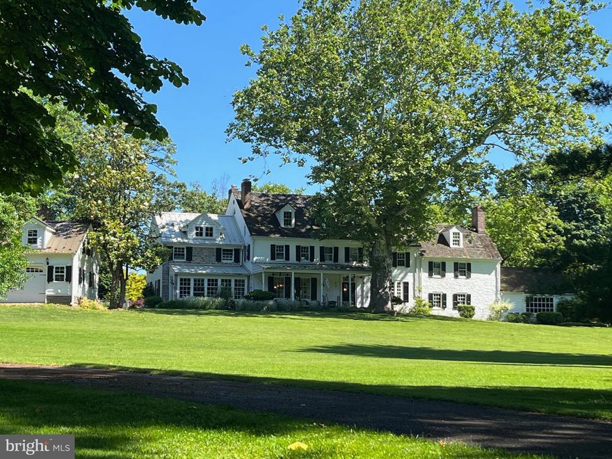 Welcome to 630 Washington Lane, a 6-bedroom, 4.5-bath Colonial residence on the historic Vernon estate in the Rydal section of Jenkintown. Dating to the 1730s, the earliest portion was established by Jenkintown founder Stephen Jenkins on land granted by William Penn—forming the historic heart from which the home evolved through expansion and refinement, including stewardship by the Newbold family who named the property in the 1800s. The home reflects a rare American provenance and benefits from modern updates, including a recent  1,000-square-foot addition that extends the home’s livability. Approached by a curving primary drive, the residence unfolds across 2.6 secluded, tree-lined acres, revealing both the main house and a newly constructed, oversized two-story carriage-style detached garage, positioned to complement the historic architecture. The grounds offer privacy, sanctuary, and estate-scale living—just moments from the heart of Jenkintown. The front door opens to a foyer with hardwood floors, chair-rail detailing, a walk-in closet, and patio access. To the right, a home office features hardwood floors, crown molding, a fireplace, built-in bookshelves, and a triple window overlooking the front grounds. Down a few steps lies the original historic core, now a billiard and game room showcasing exposed beams, hardwood floors, chair rail and wainscoting, a brick-and-stone fireplace, and built-in cabinetry. It offers access to the rear patio, a spiral staircase to the second level, and stone spiral stairs to a unique basement. Beyond the game room, the home opens into a great room with vaulted beam ceilings, crown molding, hardwood floors, and a built-in wet bar with granite countertops. French doors lead to a flagstone patio, creating indoor-outdoor flow. To the left of the foyer, the dining room features hardwood floors, chair rail, a chandelier, and a fireplace. Open to the dining room, the kitchen—designed for living and entertaining—offers hardwood floors, a two-tier island with granite countertops, pendant lighting, dual sinks, stainless KitchenAid appliances, Wolf range with pot filler, and a granite dry bar with stone backsplash crafted from the original keystone fireplace. A tiled mudroom provides access to the driveway, backyard grill area, and a flagstone patio. The kitchen opens to a family room with large windows overlooking the grounds, hardwood floors, a ceiling fan, a gas fireplace, and French doors to the driveway. A powder room completes the main level. The second-story central landing provides access to the bedrooms and west-end third story, featuring a large walk-in closet and a full bath with a glass-enclosed shower. The primary suite is a retreat, beginning with a laundry room and walk-in dressing area then opening to a vaulted bedroom with a ceiling fan and a soaking tub set into an alcove. It’s bath includes heated marble floors, skylights, a makeup vanity, a water closet, and a large shower. Three additional bedrooms on this level feature hardwood floors; two share a Jack-and-Jill bath, and the east bedroom includes a secondary staircase to the game room and access to a third-floor bonus room. Stairs to the west-end third story lead to a landing serving two additional bedrooms with hardwood floors and semi-vaulted ceilings, and a full bath with a walk-in storage room with a cedar closet. The basement includes a utility room, storage, and a partially finished area suitable for a home gym. Directly across from Abington Friends School and steps from the Abington Art Center and Alverthorpe Park, a stroll down the secondary drive leads through the Newbold/Vernon neighborhood to Jenkintown Center, with shops, eateries, and the historic Hiway Theater. Blending deep local and American history with modern updates and inviting design, 630 Washington Lane presents a rare sanctuary and an opportunity to create a true forever home in a connected and vibrant setting.