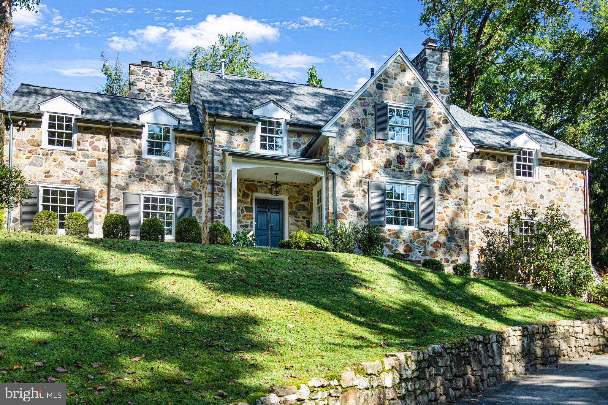 Feel right at home in this one-of-a-kind estate property located in the heart of the Main Line suburbs of Philadelphia. Nicknamed “Indian Hill,” this spacious stone home, with 5 Bedrooms, 3 full and 2 half Baths, exhibits classic, elegant original details and modernized updated conveniences. Perched on level, private, tranquil grounds and surrounded by trees and lush landscaping, this gracious home is set back from the road and accessed through original stone pillars. The floor plan is remastered and ideal for everyday living and entertaining with its well-appointed gourmet Kitchen which opens to a Family/Gathering Room. Formal rooms include an expansive Living Room with a Marble-Faced Gas Fireplace and an oversized Dining Room with an adjacent Butler’s Pantry featuring two additional dishwashers, an under-counter beverage refrigerator, and an ice maker. The charming flagstone screened-in Patio that overlooks the private grounds can be accessed through the Living Room and Dining Room. The main floor also includes a beautiful Foyer with a sweeping transverse staircase, an Office/Library with built-ins, and a 2nd Gas Fireplace. A beautiful Powder Room completes the main level. All spaces are bright with large windows, deep window sills, beautiful millwork, and random-width pegged hardwood flooring. The second floor is equally refined with 4 Bedrooms, 3 Full Baths, and a Laundry Room. The private Primary Bedroom Suite includes a large Bedroom with its own private deck, a Dressing Room with Custom Closets, and an ultra-elegant marble Bath with separate vanities, heated floors, and an oversized shower with multi-spray shower heads and body sprays. There is a second Bedroom with an Ensuite Bath and a Jack and Jill is shared between the remaining 2 Bedrooms. The third level has a fifth Bedroom with Cedar Closet. The finished lower level space with some hardwood flooring is equally useful and flexible as the oversized space can be used as a Studio, Game Room, Rec Room, or Home Theater. The remainder of the lower level is comprised of a Powder Room and multiple storage rooms. and access to the oversized 2 car Garage. Centrally located near the center of Narberth and the shops & eateries of Suburban Square shopping center in Ardmore, you will have an easy commute to Center City Philadelphia by car or rail. Enjoy this elegant home year-round with multiple patios and lush landscaped grounds. Move in and be ready to entertain family and friends for this coming holiday season.