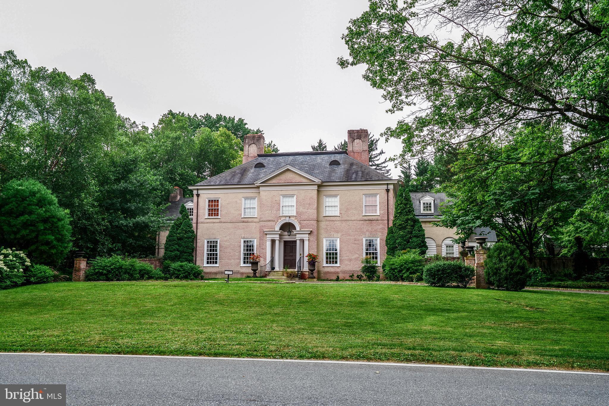 A tree-lined drive leads to the front entrance steps of the brick Georgian-style main house designed with exceptional attention to architectural detail and construction. The residence is designed to create an open and light filled warmth with 10-foot ceilings on the first floor, 9-foot ceilings on the second floor, and 14–16-foot cathedral-style ceilings with skylights and balcony on the third floor. Together, 5 bedrooms with baths, two with fireplaces and balconies, a master bedroom with separate closets and dressing areas, and 3 half bathrooms provide ample comfort for family, friends and guests. Centrally located in the School Lane Hills neighborhood, the home offers convenient access to shopping, services, recreation and entertainment.
Main house highlights include custom woodwork and built ins, a marble-tiled columned foyer, powder room, grand double height stairwell with decorative plaster accents, formal living room with antique fireplace surround and separate marble topped wet bar leads to an outdoor bluestone porch and fireplace, cypress paneled family room with fireplace, build ins, and porch access, spacious, sun filled kitchen with double sinks, custom cabinetry, high-end appliances, marble counters and travertine flooring, formal multipurpose dining room with antique fireplace, build ins, and French doors leading to private walled garden, sun room w fireplace and build ins, family entrance to mudroom with 5 custom “cubbies”, wall-to-ceiling cabinetry, separate refrigerator, soapstone counter and sink, a pantry with floor-to- ceiling storage, coat rack, stacked washer/dryer and a floor height utility sink. Lighting includes Waterford Crystal chandeliers in the dining room, custom accent lights, period-style fixtures throughout with exterior illumination provided by hand-crafted Carolina Lighting fixtures that enhance both the aesthetic and security of the property. A separate office/exercise area and powder room complete the first-floor layout. Throughout, “pocket” doors and hard wood floors provide aesthetic and practical complements for privacy and events. The second floor includes 4 en suite bedrooms, a cozy reading space, and a large central laundry, with sink, crafts center and custom build ins.
The extensively landscaped and mature plantings provide the 1.4-acre property with exceptional privacy and natural beauty. Outdoor features include an in-ground swimming pool and waterfall designed with natural elements and plantings that blend into the landscape. A spectacular blue stone slate plaza contains an enclosed seating area and fireplace and separate pool house with countertop, custom cabinetry, dishwasher, food warmers, refrigerator, and separate powder room and shower areas that together produce comfortable space for entertaining and relaxation. The three-car carriage house has a finished floor, storage systems and central vac and second floor living quarters with a kitchen, full bath, heating, cooling and central vac.
This property combines classic Georgian architectural style with modern technology and conveniences. Centrally located but exceptionally private, the mature landscaping, spacious layout, quality finishes, and integrated systems offer a rare opportunity to own a home that balances traditional design with modern systems. This property is designed to provide comfort and sophistication, suitable for everyday living as well as large-scale entertainment.