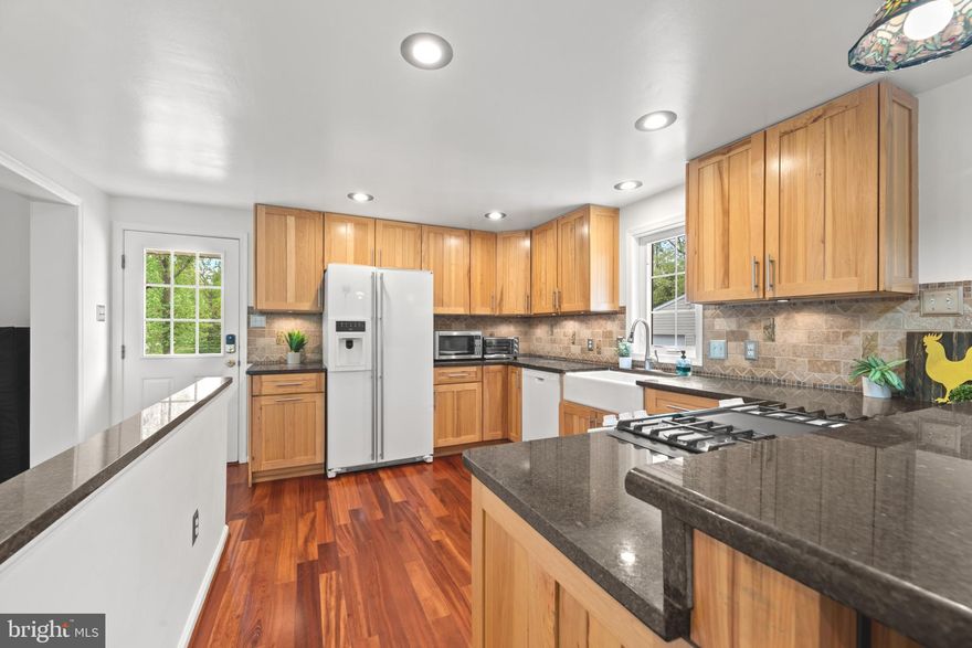 Set at the end of a quiet no-outlet street on a premium 0.46-acre lot, this well-maintained rancher delivers the rare combination of true one-level living, Howard County convenience, and zero HOA. Commuters get quick access to I-95, Route 29, Route 103, and Route 40, plus a short run to BWI.
Step inside to gleaming Tigerwood hardwood flowing through the main living areas. A sun-filled family room addition anchors the home with soaring cathedral ceilings and a wall of windows that pulls the backyard indoors. The kitchen features warm hickory cabinetry, granite countertops, a decorative tile backsplash, and a breakfast bar suited for both morning coffee and casual dinners. The living and dining combo with a bay window adds flexibility for hosting or for setting up a quiet reading nook. All three bedrooms are on the main level, including a primary with an en-suite bath.
The fully finished walk-up lower level truly lives like a second home. A spacious recreation room, a full bathroom, a full second kitchen with a brand-new stainless-steel designer range hood, and dedicated storage make it ideal for guests, multigenerational living, entertaining, or an expanded work-from-home setup.
Freshly painted interior, top to bottom. The oversized two-car garage now features a new opener and a finished bonus room in back that can be used as a workshop, home gym, studio, or private office. A second shed on the lot handles lawn tools and yard equipment. Out back, a brick patio opens to a level, usable rear yard ready for summer grilling or quiet evenings. Love to garden?  Mint, mustard seed, stinging nettles, and dill are already growing for your enjoyment.