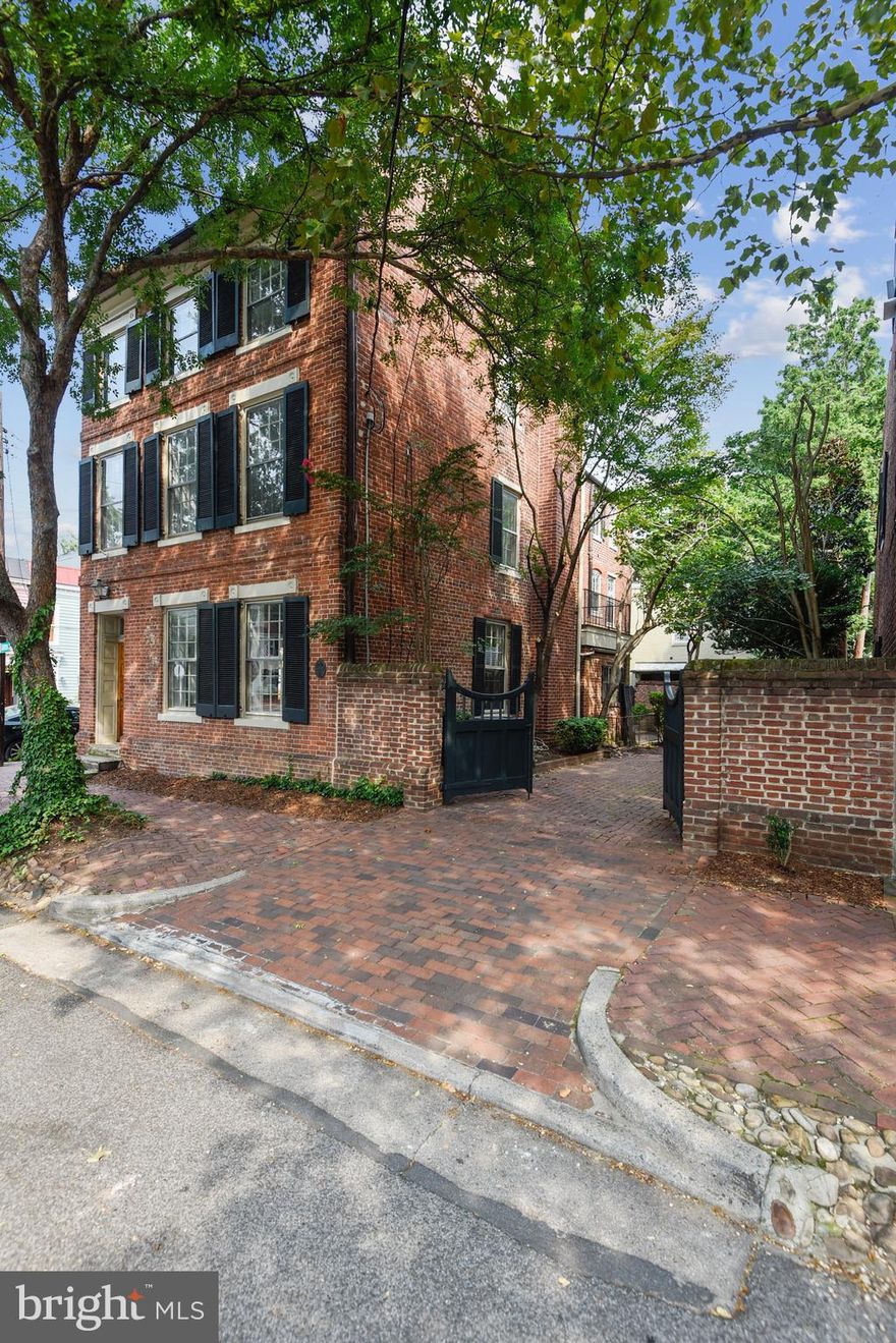 If these walls could talk, the ones throughout 221 Gibbon Street would have rich tales to tell.  Having stood the test of time and many iterations of living environments, this special residence awaits its newest steward to further the fertile heritage it has enjoyed for two centuries. Whether beginning its life as a typical early l9th century brick home with entrance hall to the side and  double parlors abutting, being enlarged  by a projecting ell at a later time,  becoming a series of  small apartments for a period of 30+ years and ultimately returning to a single family home, the gentility of the mellow  brick structure adorned with  bulls-eye  trimmed  openings  and colonial green shutters  remains.   Its deep garden with perimeter beds, mature boxwood, magnolia,  gracious yews and azalea shade and ornament the sheltered  retreat while offering 2 off-street  parking  places  through  handsome gates.  Warm heart pine floors flow throughout this light-filled residence on the northeast corner of Gibbon and Fairfax Streets while simple but traditional trim enlivens each and every room. Six rooms with fireplaces, several with surrounding hand-carved panels, are complemented by period woodwork and built-ins including several cupboards, bookshelves and window seats assuring early authenticity. A seventh decorative fireplace adds interest to one of the many bedrooms.  The main floor includes gracious rooms for entertaining including a welcoming entrance hall, double parlor and dining room, augmented by a butler's pantry. Beyond is the large kitchen with beamed ceiling, wood cabinetry and stainless appliances.   With ample room for a large table,   hours of creating  memorable  times  whether  preparing  festive  meals,  baking  cookies and  treats for the younger  set or simply  gathering  friends for lively  conversation  while  enjoying  a refreshing  beverage can be imagined.  Doors from the dining room and kitchen open to the   glorious garden making it easy to extend both casual and more formal entertaining.  Completing  this level is a unique powder room tucked beneath  the   stairs.  The second and third floors mirror each other in configuration, reflect some of the divisions made to create the smaller studio apartments and eventually were adapted to accommodate the desires of the present owners' family with six bedrooms and two sitting rooms. Each floor includes a full tiled bath and the third  floor houses a full laundry.  One wonders about the ladder in the second floor rear bedroom with its owners offering the following explanation. Having experienced the threat of fire and without a rear staircase, the family installed a unique solution to allow those at the rear of the second floor to ascend a ladder through a trap door to the third level, climb through a window to a rope ladder to the balcony below, dropping into the garden for escape. One would also guess that as the children grew older, this method would become a surreptitious way of entering and exiting the house. It is "fun facts" such as these that weave through the fabric of Old Town homes and add to their singular status.  The residence of over 4,000  finished square feet has a stone foundation basement where the  boiler is housed and at the top there is an unfinished attic. Two-zoned jet pack air conditioning maintains a comfortable temperature throughout the warmer months.  Radiator heat removes the chill in the colder ones. With close proximity to Lee Street park, the river, restaurants and shops,  this location in the southeast quadrant of Old Town is enviable while this extraordinary home anticipates  your  distinctive touch.