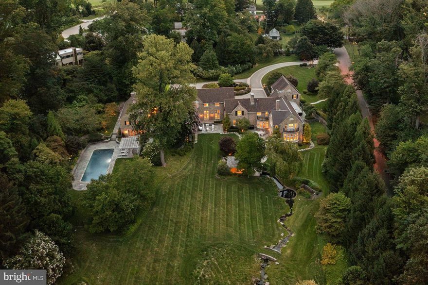 In the late 1700s, when Chestnut Hill was still many country miles outside of Philadelphia, a single-room-deep stone farmhouse was built in a valley where coldwater streams laced the forest floor. More than 200 years later, that simple stone house was seamlessly expanded by architect Peter Zimmerman into the best possible version of a classic Chestnut Hill stone home. Working with the terrain, Zimmerman created additions that blend organically into this most picturesque of settings. Beyond the immaculate parking courtyard and discreet navy blue main entry door lies a sophisticated, state-of-the-art residence. Beautifully designed for entertaining and daily living, the interior is a masterclass in color and pattern, infused with natural light and fresh energy unlike any other home in this sedate corner of Philadelphia. Interiors flow into outdoor garden “rooms,” each with a completely different feeling. Great care and much thought went into every space, from its reception area to the kitchen to its gathering spaces and private quarters upstairs. The house was completely gutted to incorporate all modern technological conveniences and amenities, including adaptive and remote lighting, temperature and security controls. Interior spaces were modernized and reorganized to accommodate lifestyle and entertaining requirements. This level of planning has resulted in a home that is aesthetically stunning and also easier to maintain and manage. The new site plan, which includes a pool, allows for sweeping views of the upper portion of the property as well as long vistas from nearly all of the interiors. As it flowed hundreds of years ago, the babbling brook is still there, well managed thanks to smart site engineering, flowing into and then out of a renovated springhouse into a large pond at the end of the property. A grass-covered stone walking bridge opens each side of the pond for long strolls around the property, creating the finishing touch to this private world that feels light years away from the city.