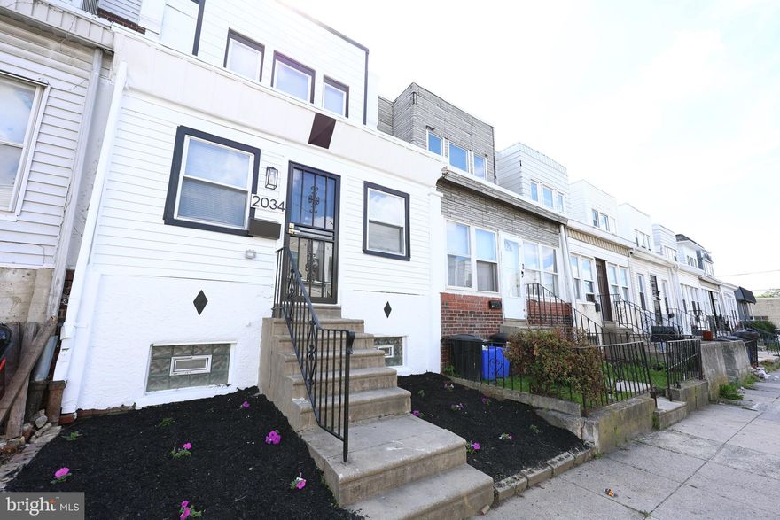 Welcome to 2034 Bonaffon St in the Elmwood Park section of Philadelphia. This beautifully updated 3 bedroom, 1.5 bathroom home features a charming inclosed front porch and modern finishes throughout. Light tone vinyl plank flooring flows through the open living space, where a sleek electric fireplace with shiplap detailing and a natural wood mantel creates a cozy focal point. The stunning kitchen boasts clean white cabinetry with brushed gold accents, a white farmhouse sink, stainless steel appliances, a center island with a sink, a stylish coffee bar with cabinets and shelving, and elegant glass pendant lighting. A custom staircase with black metal spindles adds to the home sophisticated and modern design. The master bedroom includes a striking accent headboard wall and a custom built walk in closet, while all bedroom closets are equipped with automatic lighting. The bathroom showcases modern accent tiles and high end finishes. Enjoy the convenience of electric baseboard heating with Smart WiFi Programmable Thermostats for personalized comfort in each room. The exterior of the home is freshly painted in white with black accents, and the rear yard is enclosed by a new wooden privacy fence and deck. Don't miss this incredible opportunity schedule your showing today!