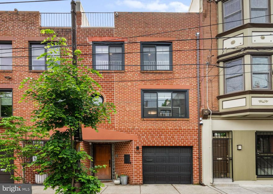 Move right into this meticulously updated and upgraded three-bedroom brick townhouse featuring sophisticated living spaces, generous storage space, an attached garage, and two levels of glorious private outdoor space.  A gated entry and custom mahogany door welcome you inside this 3,000-square-foot home filled with new white oak hardwood floors, Andersen E-series windows with updated coverings, and tall ceilings with new recessed lighting. The gracious tiled foyer offers access to your private garage, storage, and a convenient mudroom bench with cubbies. An updated oak staircase ushers you to the 20-foot-wide home's spacious living room, where the warm fireplace boasts a new mantle, tile surround, and built-ins. Enjoy seamless indoor-outdoor living and entertaining thanks to sliding glass doors that open to your private deck and backyard, with access to a large, shared courtyard. Plan elegant dinner parties in the spacious formal dining room set on a separate level. Cooking and cleaning are effortless in the beautiful pass-through kitchen featuring updated cabinetry, stone countertops, and a fleet of stainless steel appliances, including a new LG refrigerator, GE induction range, and hood, plus a dishwasher. A finished lower-level family room with a fireplace, a powder room, and a new LG washer and vented dryer with a new 240V power supply and available gas line complete the living spaces. The home's luxurious accommodations begin with a serene owner's suite offering a king-size layout, garden views, and generous closet space with new custom fittings. The beautiful gut-renovated primary bathroom beckons with a freestanding soaking tub, walk-in shower, and double vanity surrounded by beautiful large-format mosaic tile. Above, two oversized secondary bedrooms enjoy excellent closet space and a renovated full bathroom. The top floor is ideal for a home office or media lounge alongside a second powder room, a new built-in desk, and a stunning roof deck featuring unobstructed sunset and city skyline views.  This home's extensive upgrades include fresh paint throughout, solid-core doors, silver roof coating, a newer water heater, a whole-house automatic water shut-off, new exterior lights, and security cameras. Beautifully situated in a prime Queen Village location and squarely in the Meredith school catchment, this exceptional home enjoys outstanding walking, biking, and transit scores and great proximity to some of the city's best shopping, dining, and nightlife. On the surrounding blocks, you'll find the beloved Italian Market, parks and playgrounds, and a fantastic array of international cuisine. Whole Foods and Center City amenities are minutes away, and transportation is a breeze thanks to excellent bus service, the expressway, and SEPTA and PATCO trains all nearby.