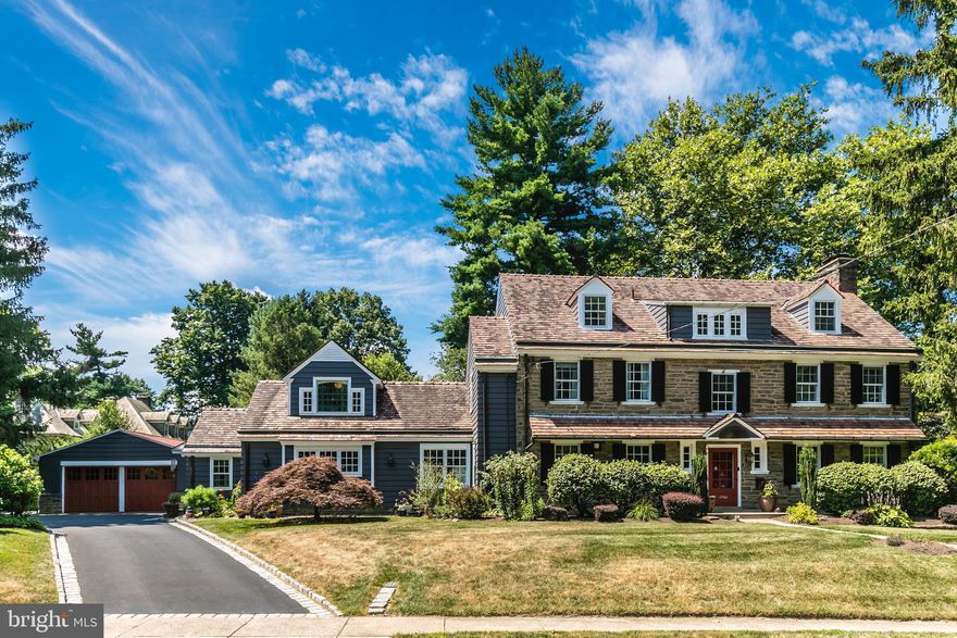 A truly beautiful and favorite Wyndmoor house with a great location.   Welcome to 7706 East Lane, a classic 1928 center hall stone colonial in exceptionally great condition on a beautiful lot close to everything.  The property is sited slightly above the street allowing for privacy and incredible views of neighboring open green space.  Wait until you see an auto enthusiast’s dream of the custom oversized 4 car detached garage – it’s fantastic and looks like a studio – with HVAC, Swisstrax flooring tile, metal workspace/storage cabinets.  The owners have loved living at 7706  and it shows by their meticulous care, quality improvements, and system upgrades including zoned heat and central air conditioning.  There are appealing home office options while still allowing for desirable living space perfect for both everyday and entertaining. Throughout the interior you’ll find generous scale, fine millwork and flooring details, great closets and storage.  An inviting front to back center hall is wide and deep and has the most exquisite stair with wide landings to second and third floors; powder room and coat closet (each with window) flank the front door, wide entry to living room, glass doors  to both dining room and sunporch, door to kitchen.  The big living room with wood burning fireplace, wall of built-ins, and glass doors to sunporch allows for flexible seating arrangements. Large, gracious dining room with elegant details, door to kitchen for sensible flow.  A rebuilt sunporch at the back of the center hall has a stone floor, skylights, many windows, glass door to back yard.  Everyone will want to gather in the expansive well designed center island eat-in kitchen with cherry cabinetry, granite counters, tile backsplash with Mercer tile accents, gas cooktop with exhaust hood, 2 wall ovens; incorporating the original butler’s pantry and great back stair.  The kitchen is open to a 2 story family room with vintage Rittenhouse Square stained glass window and gas fireplace, captivating loft space with built-in bookcases and long bench, bookcase/secret door to laundry room, tall glass doors to patio to back yard,  Right off the kitchen is a big, bright laundry room with 2 windows, counter with sink,  many cabinets.  A great looking mudroom/back entry hall off the family room has a coat closet, lovely large powder room, and door to driveway. The second floor big primary bedroom has a large custom fitted dressing room with built-ins/center bench cabinet/closet/window.  A big, beautiful primary spa-like tile bath has 2 vanity sinks, large stall shower, storage closet.   The second and third bedrooms are spacious and have good closets – one bedroom has a door to the loft over the family room which offers space for home office or meditation or perhaps a library.  Great looking hall tile bath with shower over tub and vanity sink.  Hall door to back stair to kitchen.  The third floor has 2 more spacious bedrooms each with closet – one bedroom has door to attic storage room.  Hall bathroom has a  footed tub with shower, vanity sink, tile floor.  The basement is a crisp finished plan of a recreation room with an outside entrance to steps to back yard, workshop room, studio/office with desk and built-ins and fantastic graphic flooring, gym/storage room with wall of recessed storage cabinets, and large pleasant mechanical/storage room.  The  back yard has room for play and lounging offering patio, green lawn, lovely perimeter plantings, gravel garden with raised vegetable beds,  and side English style spiral garden.  Township parks, Wyndmoor’s town center with great market and restaurants, major roads, minutes away.  More shopping, restaurants, galleries, Woodmere art museum,The Morris Arboretum,The Wissahickon/Fairmount Park, train to center city, close by in Chestnut Hill.