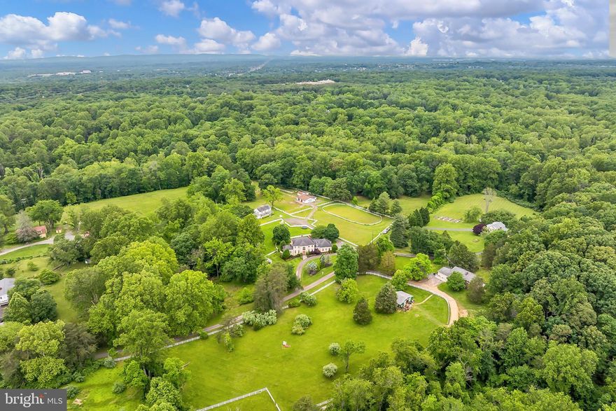 Nestled on a serene and private 6.94 acres in sought-after Clifton this unique estate offers a stately all brick 5 bedroom, 4.5 bath colonial with 4 fireplaces and plenty of living space on 3 finished levels, an in-ground pool, hot tub, a 6-stall center isle horse barn, an additional structure, two storage buildings, and multiple fenced paddock areas and a riding ring. Ideal for multigenerational living or animal and horse lovers, the property is fully fenced and offers space to grow, garden, and even raise approved livestock. ****** A private and circular driveway leads to the home where a dual door entrance welcomes you into the stunning two story foyer with a gently curved staircase, marble flooring, arched window, and a tired chandelier. The formal living room features floor to ceiling arched windows that fill the space with natural light illuminating warm neutral paint, crisp decorative moldings a floor to ceiling brick fireplace, and twin glass paned doors opening to the amazing sunroom with walls of windows. The banquet sized formal dining room offers space for all occasions, while the library makes a perfect home office. The gourmet kitchen is sure to please with gleaming granite countertops, an abundance of 42” cherry cabinetry, and quality stainless steel appliances, while the gracefully bowed breakfast area is the ideal spot for daily dining. The family room with custom built-ins and wet bar beckons you to relax and unwind in front of the 2nd brick fireplace. Sliding glass doors in the family room, sunroom, and breakfast nook grant access to the expansive sundeck with stairs to the fenced backyard area with an in-ground pool with hardscaped surround, and a hot tub—seamlessly blending indoor and outdoor living and entertaining! A powder room and a large laundry room compliment the main level. ****** Upstairs, the luxurious primary suite boasts a separate sitting room with romantic fireplace, a walk-in closet, luxurious ensuite bath, and sliding glass doors opening to a private balcony overlooking the private, lush and scenic property surrounded by majestic woodlands, the perfect spot to enjoy morning coffee or relax at the end of the day. Down the hall, a junior suite enjoys a private bath, and two additional light filled bedrooms share the well-appointed Jack and Jill bath. ****** The expansive walk-out lower level features a cozy rec room with built-in bookcases and wet bar, a huge game room with a 4th brick fireplace, a wine room with custom built-ins for wine storage, a walk-in cedar closet, and a full kitchen, and a private bedroom and bath—perfect for guests or extended family. ****** An secondary structure provides additional living space and lots of versatility. While the home is being sold as-is and features some dated finishes, it is in very good condition and thoughtfully remodeled in 2004 and 2014. With a mix of hardwood, tile, and carpet, new appliances, and plenty of room to roam, this historic and versatile estate is a rare find in Northern Virginia. Don’t miss this amazing opportunity to own a beautiful, tranquil, and equestrian estate home just minutes to the charming town of Clifton where you’ll find historic landmarks, cafés, boutique shopping, and events held throughout the year that foster a sense of community!