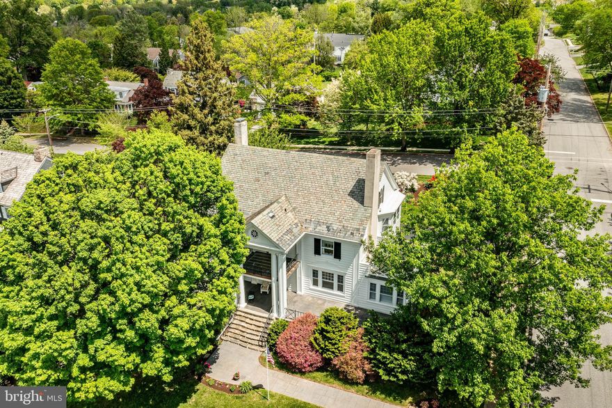 700 North Walnut may be one of the most charming and gracefully crafted homes on the market today. Set on a huge lot for the Borough of West Chester of just under one acre and nestled among mature trees and elegant neighboring properties in the sought after Northeast quadrant of the Borough, this exquisite 5-bedroom, 2.1-bath Georgian style residence is a rare blend of timeless design and rich architectural detail. Originally built in 1900, the home has been lovingly maintained and features handcrafted woodwork, triple return crown moldings, marble finishes, high ceilings and an undeniable sense of character. Approaching the home from High Street, you are immediately struck by the grandeur of the mature specimen trees, the soaring pillars, stone steps, raised covered patio, slate roof, and many windows. This is one of the grandest homes in West Chester. From the moment you enter the foyer, you are greeted by exceptional craftsmanship: crown molding with intricate profile work, bubble glass details, and a beautifully built corner hutch with an arched door crowned by a keystone. The recessed radiator tucked beneath cabinetry, a wide staircase to the upper level, and an east-facing window all set the tone for the quality and warmth felt throughout.
The formal Living Room is one of the home’s most distinguished spaces—anchored by an extraordinary fireplace with custom triple return molding, flanked by French doors that open to a luminous sunroom wrapped in nine windows. Just beyond lies the elegant Dining Room, with its arched built-ins, raised paneling, and crown molding flowing in from the adjacent spaces. Light pours in from three exposures, making this room as joyful as it is grand.
The Kitchen features rich cherry cabinetry, dual Jenn Air wall ovens, a Bosch dishwasher, and a central island with dual sinks and Corian counters—ideal for daily meals or entertaining. A nearby Breakfast Room offers north-facing windows and two custom-built desks under three more windows, with a French door leading to a peaceful covered porch. A well-organized Mud Room and Laundry area, complete with tile flooring and clever storage, add function without sacrificing style.
Upstairs, beautiful white oak floors with walnut inlays run throughout. The Primary Bedroom offers peaceful views, a large walk-in closet, and a spa-like marble bathroom with a rain shower and quartz-topped vanity. Each additional bedroom features its own charm—from the fireplace and porch access in Bedroom 4 to the sunlit expanse of Bedroom 5 with five total windows. Steam radiator heat, central air conditioning, and public utilities ensure comfort and convenience year-round. The detached two-car garage has space above for additional storage, workspace and more. The large lot provides nearly one acre of landscaped serenity. The property feels like a private sanctuary with long views, yet you’re moments from all the vibrancy of downtown West Chester and just across the street from the West Chester Country Club. 
A home of this caliber—so rich in history, warmth, and architectural integrity—rarely comes to market. 700 North Walnut is a peerless example of Borough living at its most refined.