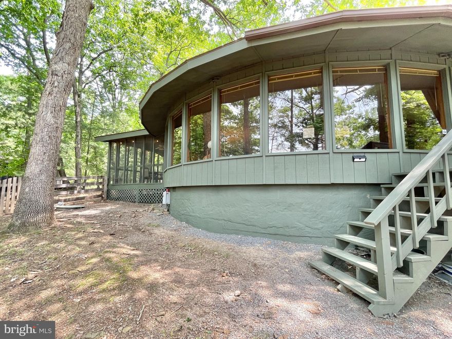 This stunning house was recently featured in the July 30th issue of the national magazine, The Week,  as their "Steal of the Week," and now it's REALLY the steal of the week with this MASSIVE $25K price reduction to $399K!  (The link to the article is provided in the agent remarks, so be sure to ask about it!!)  Listing broker is happy to discuss the short term rental possibilities with this house and is ready to answer any and all questions.  At over 2200 square feet, form and function meet and the intersection of style and substance. The Mod Pod is one of the most fabulous homes in the Woods, both inside and out.  It sits facing the golf course,  with a large gravel driveway and a two-car carport  with storage. (Plenty of room for four more cars as well.) The exterior is wooded, with a huge totally fenced backyard off of a deck and a screened in porch.  Enter the home into a generous vestibule with two storage closets and sliders off to the back deck.  Walk into the main living space where the curve of the room and the wall of the Pella double-paned windows is accentuated by the stunning real wood textured walls.  After the windows, the central feature is the wood-burning, glass, three-sided fireplace.  The kitchen is large and spacious, with all the modern touches...granite countertops, sleek black appliances and a large laundry room/pantry.  Walk down the long central hallway to the three bedrooms and two bathrooms, plus huge walk-in closet that would make a great powder room in the future. Great storage (5ft ceilings) under the house for all your seasonal decorations and yard tools, and even room for a wood shop. This house is made for family gatherings and parties - with plenty of room to sleep 8 or more and capacity for sit-down dinners for 10-12.  The roof is only six years old; the grinder pump (septic) and HVAC are brand new; the house was fully-painted inside and out; with all new carpeting. You can walk to the pool and the Woods Grille. This house has a membership to the gym and the pools for an additional $1500 a year and includes three pools (one indoor and two outdoor, indoor and outdoor tennis, pickle ball, spa and fitness center  Monthly HOA dues are $66.67 per month. House is currently being rented short term, and is available to show August 13th-18th at all times, and after August 27th.  Listing agent will open the door and accompany at showings.