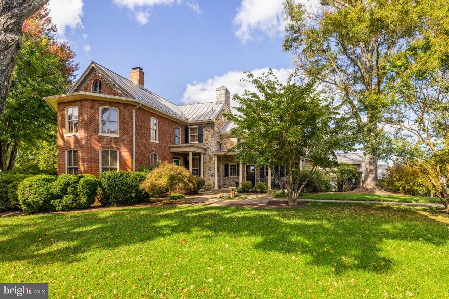 On a picturesque country lane, in the foothills of the magnificent Blue Ridge Mountains, this exquisite Quaker style stone and brick residence, circa 1780, presides over 12.7 gorgeous acres of lush fields, sweeping lawns and brilliant perennial gardens offered with two parcels. Towering trees, stone walls and breathtaking views create a magical setting for this exquisite historic home, which has been meticulously restored, beautifully updated and elegantly appointed. The manicured grounds include a charming Guest House, with a new kitchen and sparkling new bath, and a fabulous heated pool, with a stone walled fountain and fieldstone terraces, completely secluded by the gardens and mature landscaping. In addition, there is an extraordinary four bay garage, a showplace for treasured cars and an incredible workshop that is anyone’s dream. There are two impressive driveways accessing the estate. The main entrance brings one to a terraced stone walkway leading to the formal front entry and the elegant foyer of the 1850 Queen Anne style wing. High ceilings, intricate moldings, travertine flooring and a lovely oak staircase are featured here, with a guest powder room located towards the rear. To the left is the stunning formal living room with gleaming wood floors, a wood burning fireplace and multiple large windows, bathing the room in natural sun light. To the right of the foyer, one enters the handsome family room, which is part of the 1824 stone addition. When originally built, this section offered the stately front entry, which now faces the mountains and enjoys a circular drive and spectacular vistas to the West. Brilliant crystal chandeliers, crown moldings and elegant mirrors grace both of these gracious rooms. Adjacent is the cozy tea room and a rear hallway with stairs to both the upper and lower levels. This addition then opens into the original section of the residence, which dates back to 1780. Originally a two over two stone home, a wall was removed on the main level creating what is now the very charming formal dining room, with wide plank pine floors, deep set windows, a stone fireplace and doorway accessing the beautiful front gardens. From the dining room one steps down into the gourmet country kitchen, completely remodeled and boasting a fabulous Lacanche five burner gas range, new refrigerator, farmhouse copper sink, Cherry cabinets with mirrored insets and the kitchen floor has radiant heat. In 2010, a mudroom was added with wonderful pantry space, slate flooring and a covered porch, leading out to the spectacular gardens, a stone smoke house, the guest house and heated pool. From the main stairwell one ascends to the second level, and to a spacious and light filled bedroom/sitting room with an inviting brick fireplace. An elegant hall bath, a huge master bedroom with wood burning fireplace and a dressing room and custom closet built-ins are located here. From the rear stairwell, one has access to both the master bedroom and to the two rooms of the original 1780 section, now a study, full modern bath and sitting room. Continue up the staircase to the third level, featuring a study/bedroom and another full bath. The second tree lined driveway entrance, offers access to the absolutely charming and very inviting guest house, and the new custom built four bay garage. Anyone with a fondness for vehicles with either 2 or 4 wheels will appreciate the outstanding features of this very special building. Strategically located below the view shed of the home, it was built to minimize its footprint with two bays facing south and two bays facing east, joined together by a corner work area with custom built-in work counter, a wet bar and an extra wide stairway providing excellent access to second level storage. The concrete floor, with radiant heat, is coated with an epoxy finish and equipped with floor drains. With interior hot and cold water connections, cars can be washed year round.