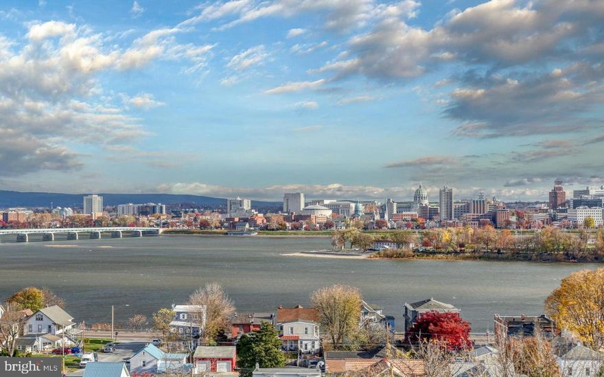 Expansive, 12’ floor-to-ceiling windows frame unrivaled panoramic vistas where the outstretched Susquehanna River casts reflections of the elegant arched bridges and dramatic Harrisburg city skyline. This exceptional backdrop transforms daily. On a clear day, it can go from a sensational sunrise to an early evening magic hour that casts the golden rays of sunset onto the tall glimmering buildings. Not to be unmatched by the sparkling display of city lights as night falls. An entertainer's dream, the seamless indoor-outdoor flow extends to a brick patio, perfect for soaking in these million dollar views. Built in the early 90’s, the one owner pride of ownership is evident. With an elevator that serves over 3,100 SF of luxurious living space, it's easy to understand the benefits and desirability. Ceramic tile and gleaming hardwood floors cover the entire main level. Two story, open staircase with dual turned volutes with white painted spindles from the oak railing to the oak treads. Formal living room with built-in solid cherry cabinets, shelves, and desk doubles as a study. Avalon inspired kitchen design is as light and crisp as the beach air featuring newer GE stainless steel smoothtop range with dual oven, built-in micro, matte finish stainless steel GE Profile refrigerator included. Pull outs in the pantry and lower cabinets, glass mullion doors, two tiered peninsula. Corner sink with pass thru to formal dining room and gorgeous river and city views. Wide crown molding and extra wide chair rail woodwork detail the elegance of the dining room. Retire to the 12’ great room and the remarkable wall of windows featuring an open gas log fireplace with opulent marble surround and painted wood trimmed wall. The gas fireplace could easily be converted back to a wood burning fireplace. Or, mix yourself an Aperol Spritz in the hidden bar and step onto the brick patio for a rejuvenating wind down to your day. Upstairs, the primary ensuite enjoys the same spectacular views. The five piece bath features a double bowl vanity, tile shower, and a walk-in soaking tub. You read that right, a walk-in tub with a seat for a comfortable, relaxing bath. There are also two enormous walk-in closets and patio doors with a wrought iron faux balcony. Two additional, spacious bedrooms, a large tile main bath, linen closets, and convenient second floor laundry. The finished lower level is one big, open room. Enough space that could be separated into a media room and home gym. There is even a rough in for another bath. Plus, lots of extra storage space in the unfinished lower level or in the detached, extra large two car garage that connects to the home via a covered breezeway and brick service walk. Privacy fencing, lawn and landscaping lead to a wide, brick stoop. All of which creates a warm and welcoming courtyard. This prime location, carefree living, and sensational city and river view make this very rare opportunity a highly sought after place to live. Call today to schedule your private tour.