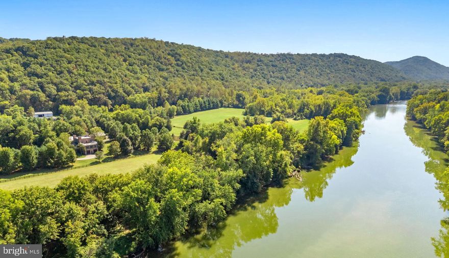 Unmatched in its 1.7 miles of river frontage, 224-acres, prime location, and estate home, every adventure is within reach here, whether hiking, fishing, hunting, hobby farming, equestrian pursuits, or simply savoring days along the river.
Just 90 minutes from Washington D.C., framed by the Shenandoah River and Blue Ridge Mountains, Idlewild’s land stands apart in its beauty, scale and diversity. Along the Shenandoah River, 120 acres form a private frontage ideal for riverside walks or trail rides. Cleared paths lead to swimming holes, shaded picnic spots and quiet banks where the sound of water over the shoals restores calm.
Between the river and the house, rich pastures unfold. Scenic and functional, the fenced fields are ready for horses or livestock. Across Howellsville Road, 100 wooded acres rise to a ridgeline at 800-feet of elevation and offer extensive trails for hunting, riding, hiking or ATV adventures.  
Idlewild’s residence, reconstructed in 2009, has been beautifully built anew. Sitting on the original site, the stately Federal-style brick home maintained the exterior style of the historic Idlewild home, built circa 1853. With 4,000 square feet, 4 bedrooms and 4.5 baths, the residence is perfectly sited between river and mountains, overlooking a large pond with a Blue Ridge Mountain backdrop.
Wide porches span the front and rear elevations, connecting the home with the surrounding countryside. Inside, rich hardwood floors anchor an open plan in which the living room flows into the dining area and kitchen, creating a warm and inviting atmosphere. Oversized windows frame views of the pond, pastures and mountains. The main-level primary suite, added in 2012, offers both convenience and privacy, with a large walk-in closet and a spa-like bath featuring a clawfoot tub, glass-enclosed shower, premium finishes and hidden laundry.
Upstairs, three additional bedrooms include a generous ensuite with peaceful views. From this level, step onto the roof deck, an inspired space for lounging or soaking in the hot tub while overlooking the river and fields. The lower-level blends utility and design with high ceilings, slate floors, a full bath, kitchenette, and stone fireplace. This casual living space can flex to a gym, studio or home office, complete with Starlink connectivity.
Elements of Idlewild’s history have been carefully preserved and reimagined. The covered breezeway that once linked the kitchen to the main house has been repurposed as an inviting space for al fresco dining. Bricks from the original 1850s home—kiln-fired on the farm—were repurposed in the Carriage House, now a detached garage with a farm office. The former estate kitchen has been transformed into a charming one-bedroom, one-bath guest house, while the original corn crib stands a restored antique. At the river near the modern bridge, remnants of the 1920s Byrd Bridge still stand, reminders of the travelers and commerce that have passed through Berry’s Ferry since the early 1800s.
If seeking an estate of rare character and scale, Idlewild River Farm possesses the best of Virginia’s countryside. Live among historic estates such as  Long Branch, The Tuleyries, and Carter Hall. Enjoy local restaurants, wineries, breweries and golf courses with quick access to Rt 340, Rt 7, Rt 50 and I-81. Located 20 minutes from Winchester and Front Royal, 45 minutes from Middleburg and just 90 minutes from Washington, D.C.