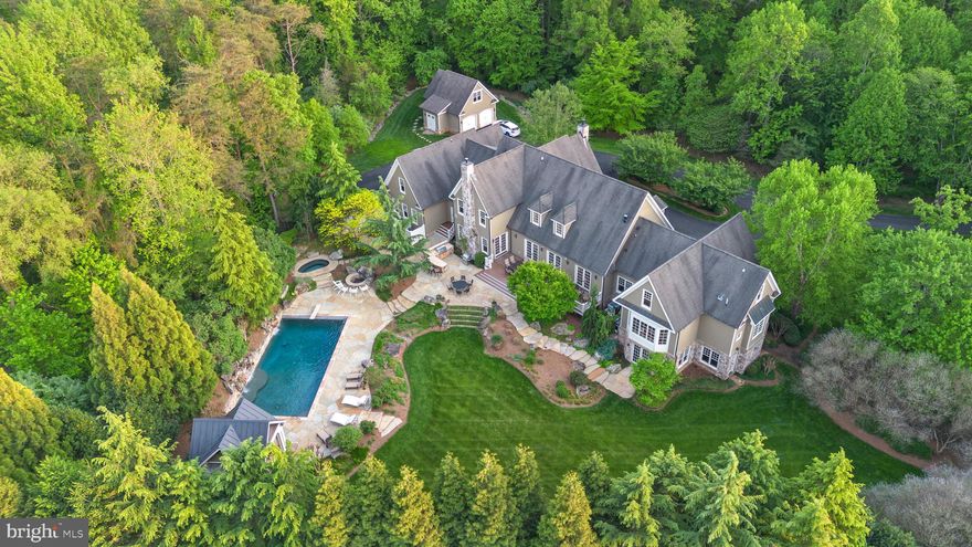 Welcome to this stunning custom-built estate on 5 tree-lined acres—an entertainer’s dream with a backyard paradise that feels like a private resort. Featuring a 22’ x 44’ rectangular pool, stone patios, a pavilion for covered lounging, and multiple spaces for outdoor dining and entertaining, this home offers unmatched indoor-outdoor living surrounded by mature landscaping and total privacy.

A long driveway winds through the wooded setting and leads to a grand circular drive. The exterior blends timeless charm with stone and cedar siding, setting the tone for what’s inside.

Step into a bright two-story foyer with coffered ceilings, chair rail, picture frame wainscoting, and elegant wood-trim accent walls. Adjacent is a formal sitting room with a stone gas fireplace and backyard views. Next to it, a double-story office finished entirely in oak offers a stunning library-like retreat with floor-to-ceiling wood, built-in shelving, and a staircase leading to a unique bonus room—ideal as a creative entertainment space or another bedroom.

The kitchen is the heart of the home, adjacent to the living area and separated by a striking arched opening. On the other side is a sunroom with a gas fireplace and French doors that open to the rear deck. Both the kitchen and sunroom overlook the backyard’s lush trees and pool. The kitchen features custom Brookhaven cabinetry, a Wolf 6-burner gas range with pot filler, Sub-Zero 36” paneled fridge, double wall ovens, and a walk-in pantry with Wood-Mode built-ins, a Sub-Zero wine fridge, and second dishwasher.

The main-level primary suite is a peaceful retreat with a large bay window overlooking the pool, two walk-in closets with wood built-ins, and a spacious bath—bright, airy, and private.

Upstairs offers five additional bedrooms, a loft area, and a bonus room with an office—ideal for guests, hobbies, or extended family.

The walkout lower level has two staircases and endless possibilities: an entertainer’s bar with dishwasher, mini fridge, and appliances; a climate-controlled wine cellar with built-in cubbies; and a theater room with surround sound and multi-level seating. A spacious bedroom with en suite bath overlooks the pool—perfect for guests.

The backyard is a showstopper. The large pool features two stone waterfall elements and a built-in ledge for in-water seating beneath the cascades. Nearby are a stone-surround jacuzzi, a fire pit area, and an outdoor kitchen with a stone exterior, built-in bar seating, and grill. A vaulted-ceiling pavilion with a stone feature wall and multiple patio areas complete the resort feel.

For car enthusiasts, the property includes seven garage spaces: an attached four-car garage with floor-to-ceiling built-ins, and a separate three-car detached garage with a finished upper-level workshop.

Located just 5 miles from Great Falls Village and minutes from Route 7, the Dulles Toll Road, Tysons, and D.C., this home offers both privacy and convenience. Zoned for the award-winning Langley High School pyramid.