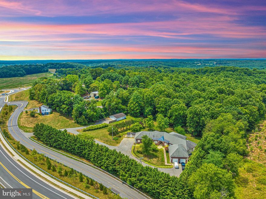 Welcome to a sophisticated blend of rural tranquility and elegant living. This breathtaking custom rancher offers over 8000 square feet of meticulously designed interior space and sits on a sprawling 5.7-acre lot. With four spacious bedrooms and four and a half bathrooms, this residence is an epitome of comfort and versatility. Prepare to be amazed as you enter the grand living room, highlighted by 12-foot ceilings, stunning built-in bookcases, and a cozy gas fireplace. The dining room, office, and foyer are adorned with exquisite custom made Black Cherry floors, adding a touch of classic elegance to the home.
The gourmet kitchen is a chef’s dream, equipped with granite countertops and a spacious pantry. Adjacent to this space, a huge sunroom offers panoramic views of the lush, surrounding landscape. For entertaining, the fully finished basement includes a second kitchen, a large bar with mini refrigerators, and a sink. This space also offers a private entrance, making it perfect for guests.
Emphasizing accessibility, this home is fully handicap accessible, featuring an elevator and wide hallways. The primary bedroom serves as a private retreat, complete with a large ensuite bath and walk-in closet. The second bedroom also boasts its own ensuite bath, while all bedrooms feature walk-in closets, providing ample storage for everyday living.
The outdoor area is equally impressive. The large deck at the back of the house provides an ideal setting for gatherings or quiet relaxation. The property also includes a large, heated, and insulated building, perfect for a workshop , machine storage or an awesome man cave or she shed.
An oversized two-car garage on each side of the home offers a total of four garage spaces, ensuring ample room for vehicles and equipment. Ideal for someone looking to generate rental income, the property includes a tenant house with rental potential of $1800 per month.  This property combines luxurious living with excellent income producing opportunities. Only two miles away from Interstate 270, the property provides convenient access to nearby amenities while preserving its private, secluded ambiance.
The picturesque Black Hill Regional Park is in close proximity, providing endless recreational opportunities.