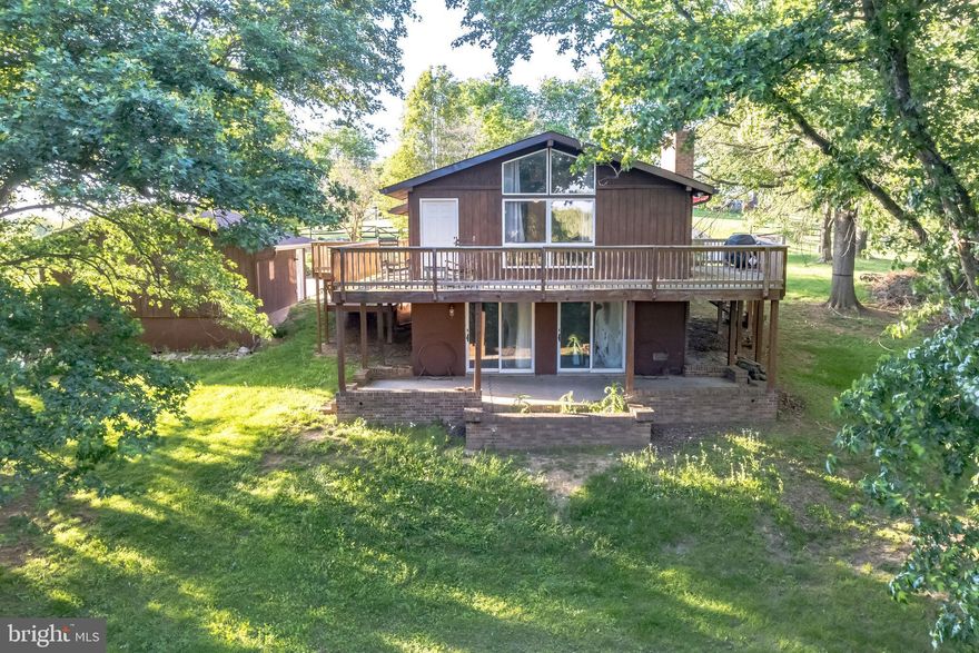 Welcome home to this rustic Colonial backing into trees on 1.5 acres of land in peaceful Cool Hollow Estates! Plenty of space to grow in this 3 bedroom, 2 bath home with an extra large garage that doubles as a workshop! You'll love the tree lined views, and rural landscape - your very own getaway. Walk into a light and bright home that features a cozy cabin getaway aesthetic. The spacious living room features wood paneling on the walls and ceiling, exposed beams, and a 9 ft+ vaulted ceiling. Stay warm next to the brick front wood burning fireplace with mantel and hearth. Entertain guests easily in the formal dining room with four light chandelier and peaceful view through the sliding glass doors leading to the upper level deck. The kitchen features plenty of counter and cabinet space, double sink with window view, and all white appliances, including a fridge with pull out freezer. Easy living with all bedrooms and bathrooms on the main level. All three bedrooms feature plush carpeting, cooling ceiling fans, and large closet spaces. Primary bedroom suite features bathroom with tub/shower combo. Another full bath completes the level. Take the winding stairs to the finished basement that's perfect for an additional living area or rec room and features shiplapped walls and another cozy wood burning fireplace and a rough in for bath. Large storage room features a full size washer and dryer. Sliding glass doors in the basement lead right to the patio and spacious backyard - the perfect place for warm summertime entertaining. Enjoy the views on your wrap around deck. Amazing private location but still close to major commuting routes - the best of both worlds! Minutes away from Hagerstown Premium Outlets, shopping and dining. Do not miss out on this one!