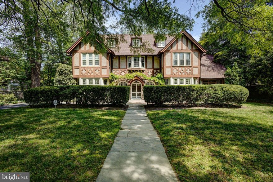 Tucked beside a historic 19th-century stone wall in the heart of Chestnut Hill, 8031 Seminole Street is a timeless residence that is a masterful blend of Tudor Revival charm with Colonial elegance. Designed in 1916 by renowned architect Robert R. McGoodwin as part of Dr. George Woodward’s visionary plan for an artfully crafted community, the home is a testament to enduring craftsmanship and architectural grace. Set on 0.63 acres and embraced by flowering gardens and mature trees, including cherry blossoms, magnolias, Japanese maple, dogwood, birch, hawthorn, and cherry, this is more than a residence; it’s a private, living piece of Chestnut Hill history.
The stone exterior is accented with decorative half-timbering, steeply pitched gable roofs which capture the essence of Tudor Revival design. The Colonial influence is evident in its symmetrical layout and classical proportions. Herringbone brick pathways weave through the gardens, leading to flagstone patios ideal for hosting under the stars or enjoying a quiet morning surrounded by birdsong and blooms. Even the detached garage is thoughtfully styled to complement the home’s historic character. Cascading wisteria frames the arched stone entry, leading to a triple-arched front way and Mercer-tiled mudroom/vestibule, complete with a stone fountain and basin that sets a tranquil tone. Inside, the home unfolds graciously across 6,831 square feet with seven bedrooms, and five bathrooms, offering a layout that is functional as it is beautiful.
A spacious foyer welcomes you to beautifully finished hardwood floors and stunning windows throughout the home overlooking the trees and landscaped views. You’ll always enjoy the sunshine as the home receives generous east/west sunlight throughout the day. The main level opens with a grand foyer, where sunlight dances across hardwood floors and oversized windows frame views of the lush gardens and trees. There is also an ample front hall closet with a doorway to the back patio. A formal living room with a wood-burning fireplace and French doors opens to an enclosed flagstone porch. A sun-splashed dining room overlooks the front gardens, while a cozy family room with built-ins invites intimate evenings at home. The step-down half bath combines unique style with everyday functionality which is perfect for both daily use and entertaining. At the heart of it all is the chef’s kitchen with a rear mudroom. The kitchen features a butler’s pantry, quartz island with cooktop, glass-front cabinetry, and breakfast room with windows that open onto a storybook courtyard.
Upstairs, two separate staircases lead to the home’s private quarters. On the upper levels, you'll find seven bedrooms, three full baths, and a half bath with a thoughtfully placed laundry area for modern convenience. The primary suite is a restful retreat, with an ensuite bath and a custom walk-in closet with additional access to an office. Throughout the home, original details and charm abound with pocket doors, rich millwork, arched doorways and built-in shelving.
8031 Seminole offers a rare blend of architectural distinction and breathtaking natural surroundings. Just steps from charming shops, acclaimed restaurants, top-rated schools, the scenic Wissahickon trail, and with easy train access to Center City and Manhattan, this is where historic charm meets modern lifestyle. Come experience the warmth, beauty, and history of 8031 Seminole Street for yourself. This extraordinary home is one you simply must see to believe. Don’t miss the chance to make a timeless piece of Chestnut Hill your own.