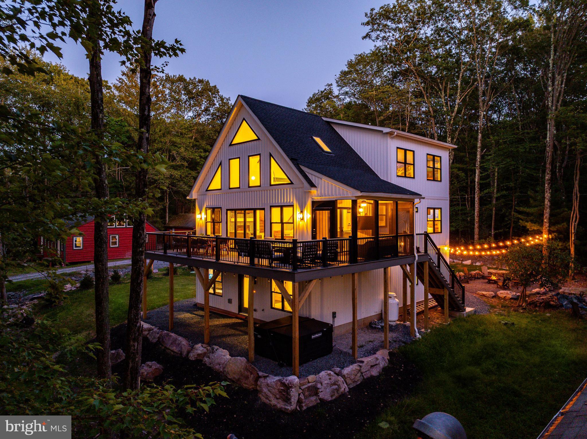 Step inside a Custom Modern Rustic Retreat where design, nature, and comfort collide. Built in 2025 and fully furnished with PUBLIC SEWER and NO HOA, this raised chalet was crafted to deliver an unforgettable experience, blending bold style with biophilic design that brings the US National Parks to your door step. Whether you are looking for your dream mountain to enjoy with family or friends or an investor looking to Airbnb (projected gross income of $200,000+) this home is a must see. From the moment you enter, you’ll notice the soaring ceilings, striking wall murals, and oversized black-on-black Andersen windows that flood the home with light and frame serene lake and forest views. The open-concept main level (2nd floor) is anchored by a tiled herringbone wood-burning fireplace, 2 skylights, and a gourmet kitchen featuring matte green cabinetry, white GE Café appliances, gas cooking, white quartz countertops, and designer gold hardware. Unique elements like the hanging canoe centerpiece and retro arcade machine make this home as playful as it is luxurious. With six spacious bedrooms, four full bathrooms, and a versatile gym/office, there’s room for everyone to spread out — whether it’s families, friend groups, or guests seeking a true escape.
Outside, the property’s outdoor oasis is built for connection and relaxation. Accordion-style doors open to a Trex deck with dining space, a fire pit, and a hot tub tucked below. A screened-in porch offers year-round enjoyment, while thoughtful amenities — like a dedicated bunk room, oversized Tic-Tac-Toe game, and loft for reading or gaming — ensure fun at every turn. Additional features include Aqua Guard Luxury Vinyl Plank flooring, a Tesla charging station with eight-car parking, 3-zoned HVAC, tankless hot water heater, brand-new well, and public sewer.
All this, just minutes from Big Boulder Ski Area, Hickory Run State Park, Split Rock Resort, Pocono Raceway, Jack Frost National Golf Club, and H2Ooooh! Indoor Waterpark. Dining hotspots like Nick’s Lake House, Louie’s Prime, and Shenanigan’s are around the corner, and with quick access to the PA Turnpike and Route 80, the adventure continues year-round. This home isn’t just a place to live — it’s a mountain-meets-modern retreat designed for making memories.