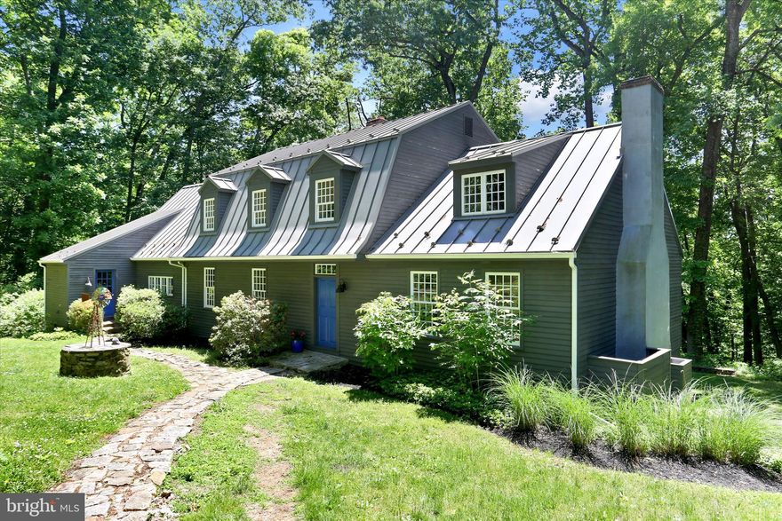 Nestled at the end of a completely private driveway on a breathtaking 5-acre parcel in desirable West Vincent Township, this stately Dutch Colonial offers a rare blend of seclusion, character, and convenience within the Owen J. Roberts School District. Surrounded by rolling meadows and mature trees, the setting feels like a private retreat while remaining just minutes from Marsh Creek State Park, French Creek trails, charming local restaurants, farm markets, and the vibrant villages of Chester Springs and Birchrunville. A newer metal roof crowns the home, adding both timeless appeal and durability.
Step inside the spacious foyer and immediately appreciate the extraordinary mission-style wainscoting crafted from reclaimed wood salvaged from a historic Philadelphia bar.  No expense was spared with beautiful wide plank hardwood floors throughout.  The sun-drenched living room welcomes you with a hotel lobby size and vibe, including a stunning central fireplace and abundant natural light. Across the rear of the home, a cozy office with a wood-burning stove creates the perfect workspace with peaceful views and warm ambiance. The office flows seamlessly into the dining room, where newer French doors open onto the expansive rear deck. The country kitchen overlooks a generously sized great room featuring another fireplace, walls of windows, and direct access to the deck, all framed by tranquil wooded views.
Upstairs, the thoughtfully designed primary suite features a unique split bath layout for privacy and comfort. One side includes a private room with a gorgeous brand new walk-in shower, sink, toilet, and closet, while the opposite side offers a soaking tub, separate sink, and an oversized walk-in closet. This primary suite hallway is also home to another large walk-in closet/room that could be a nursery or full laundry room.   Two additional bedrooms, hall walk-inn closet and another full bath complete the upper level. Stretching across the back of the home, the sun-dappled deck is partially shaded by a lush, plant-covered pergola, creating an idyllic setting for entertaining or quiet relaxation. The walk-out basement  with radon remediation system remains unfinished and ready for your vision, offering endless possibilities for additional living space, recreation, or storage.   A standout feature of the property is the impressive detached garage added in 2014, showcasing beautiful natural wood finishes and exceptional craftsmanship throughout. Designed with both functionality and style in mind, the extra-long and extra-wide two-car garage offers ample space and ceiling height to comfortably accommodate two full-size trucks. In addition, a separate equipment garage with its own automatic garage door provides the perfect space for tools, lawn equipment, recreational vehicles, or workshop needs. Stairs lead to a spacious second-level storage area complete with windows, creating a bright and versatile space ideal for storage, hobbies, or future customization.  Property is in  French & Pickering Creeks Conservation Trust. Generator is fueled by a leased propane tank (Styer Propane).  GPS  is using Spring City rather than Chester Springs.