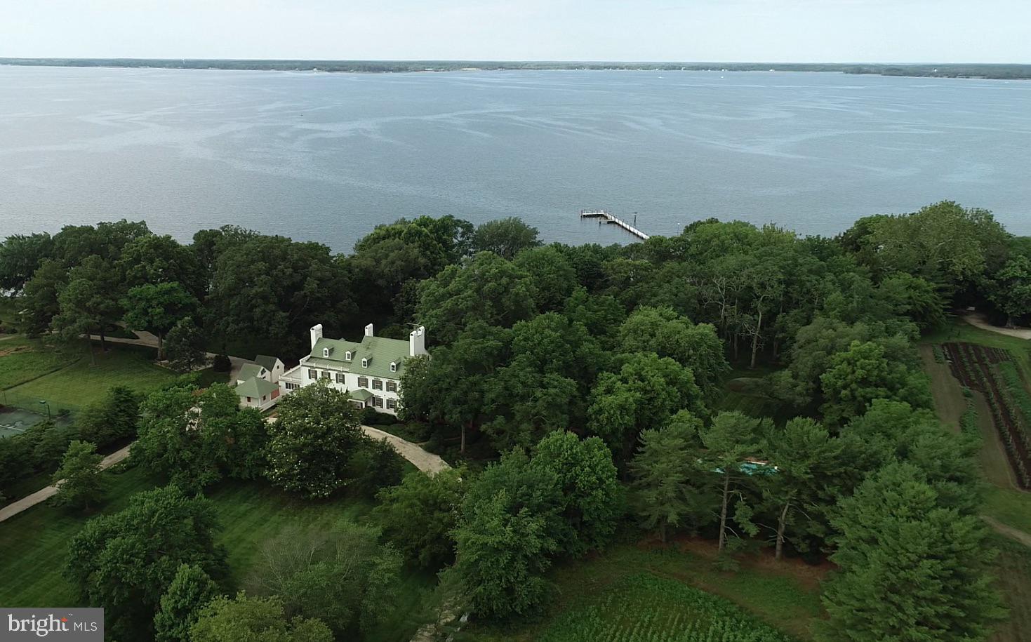 Wilderness Estate- REVISED OFFERING INCLUDES 5 PARCELS 6.27.25- This quintessential Eastern Shore farm is located along the Choptank River in Trappe, Maryland. Comprised of 234 acres, with original structures that are impeccably well-kept and improved with modern amenities, The Wilderness provides a unique opportunity to enjoy the best of the Eastern Shore. Surrounded by open space and preserved farmland with proximity to Oxford, Easton, Cambridge, and St. Michaels, The Wilderness is sure to please the discerning buyer.
Sited among large waterfront estates, The Wilderness enjoys privacy and a commanding presence with old-growth trees, broad southerly views, and deep water. The scope of improvements includes the primary residence, waterside guest cottage, beach house, pool, pier, tennis court, early 20th-century barn, and a host of accessory structures for life on the farm. Visit the virtual tour for an inside look and appreciation for the scope of this offering.
The main house has great historical significance not only for the original owner’s grandson who lived there and served two terms as the Governor of Maryland but also for its place in the development of Maryland’s domestic architecture, as noted on two markers from the Maryland Bicentennial Commission and the Maryland Historical Society.
The smaller and original of the two brick wings dates from the late 18th century and the larger wing from the early 19th century. The house’s architecture is unusual in that the 19th-century wings telescope up, instead of down, from the original wing. The white brick, black shutters, and historical olive green trim color are a serene palette against the house’s majestic specimen trees around the property, including a gigantic Sycamore that is the largest of its species in Maryland.
The long white gravel drive under the sheltering canopy of mature trees passes by the barn and other outbuildings then curves around the front of the house. Brick steps lead up to the front porch of the early 19th century wing opening into a gracious foyer and stair hall with an elegant elliptical arch that rests on pilasters at the side walls to separate the public from private areas of the house. A French door at the rear of the foyer frames a vista of the lawn and Choptank River. To the side of the foyer are two identical parlors at the front and rear corners of the house. Both rooms have magnificent fireplace mantles and surround; one is a 1740 hand-carved mantel by noted English artisan woodcarver Grinnling Gibbons and the other is a 1780 mantel surrounded by the famous English architect and artisan, Robert Adam.
The main floor of the 18th-century wing contains a spacious living room, dining room, original kitchen, and larger kitchen, pantry, two powder rooms, and a stunning sunroom connecting to a terrace along the rear of the house overlooking the Choptank River. Part of this wing was the final addition to the original home.
The second floor of the 19th-century wing contains two bedrooms over the two parlors below with fireplaces and walk-in closets and two baths. The 18th-century wing and later addition contain an artist’s studio with cabinetry and sink that has a myriad uses– TV room, arts and crafts room. The primary suite is located at the rear corner of this wing. It has a fireplace flanked by single windows and another window on the rear wall for panoramic views of the mature landscape and the Choptank River. Two baths complete the suite, with one bath off a hall for access from the art studio.
Two stairs access the attic level; one in the 18th-century wing leads to two bedrooms and one bath. The main stair in the 19th-century wing leads to a large game room and another cozy bedroom ensuite.
The revised offering of The Wilderness, providing 234 acres comprised of 5 recorded parcels with over 3,000 feet of shoreline is a remarkable opportunity to witness life on the Shore.