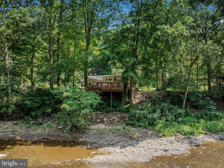 This property offers an ideal setting to appreciate the Cacapon River, with the soothing sound of flowing water creating a serene ambiance. The cabin boasts an enclosed porch, living room with a sleeper sofa, kitchen, bedroom, and bathroom. Additional amenities include a deck and covered porch perfect for relaxation. A bunk house is available for accommodating guests, and an exterior bathroom provides convenient access for showers. A carport is also available for campers, complete with a 30-amp breaker and water hookup. The cabin is fully furnished, allowing guests to simply bring their bathing suits, fishing gear, and kayaks to enjoy the river life.   Steps lead directly to the river, providing easy access.   Property being sold as is.