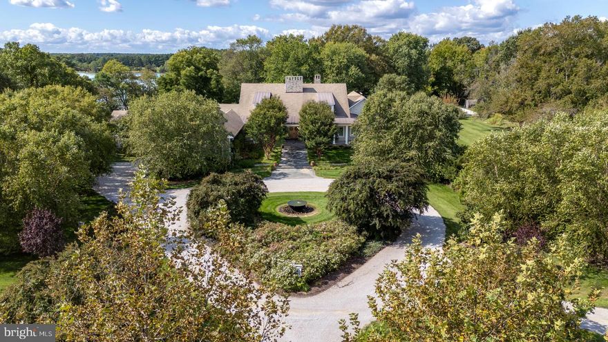 Set along the peaceful waters of Caulk Cove, this extraordinary waterfront estate offers luxury, privacy and natural beauty across more than 10 acres. The property features open farm fields and professionally landscaped, park-like grounds, with a tree-lined driveway creating a breathtaking approach to the residence. Built in 2013, the custom-designed home encompasses nearly 8,500 square feet of thoughtfully curated living space, positioned to capture sweeping waterfront views. A gracious front porch welcomes you into a grand foyer, setting the tone for the exceptional craftsmanship found throughout. The main level offers soaring 12-foot ceilings, rich hardwood floors, expansive windows and doors and custom millwork including crown molding, coffered and tray ceilings and elegant board-and-batten detailing. At the heart of the home, the living room serves as a remarkable gathering space with a dramatic floor-to-ceiling stone fireplace, custom built-ins, coffered ceilings, a wet bar and access to the rear porch. The kitchen is a stunning focal point, featuring a diamond coffered ceiling, custom handmade walnut cabinetry, two oversized islands, white and leathered granite countertops, and a Wolf six-burner, dual-oven range. A fully equipped butler’s pantry offers extensive cabinetry, generous counter space, a secondary refrigerator, dual dishwashers, a wine refrigerator and an electric oven. The open dining area flows seamlessly between the kitchen and living room. The primary suite is a private retreat with a tray ceiling, wood-burning fireplace, expansive walk-in closet with custom built-ins and vanity and a luxurious bath featuring heated floors, a jetted soaking tub, separate vanities, an open tile-and-glass shower and a private water closet. The suite is completed by a private sitting room with fireplace and wet bar, along with a private screened porch overlooking the gardens and serene waterfront. Four additional ensuite bedrooms each offer unique and luxurious bath designs. A well-appointed laundry room with ample cabinetry and generous counter space enhances everyday convenience and leads directly to a functional mudroom with access to the attached two-car garage. The second level features 9-foot ceilings and is anchored by a spacious family room with a stone hearth wood-burning fireplace and built-in window seating, flowing into a billiards area with wet bar, creating an ideal space for entertaining. The sixth bedroom currently includes custom built-in bunk beds but was originally designed as a home office and offers flexibility to be restored to its original use. The home’s exceptional design extends seamlessly outdoors, with a spacious screened porch leading to an open-air porch with a wood-burning fireplace and outdoor entertainment setup. Bluestone walkways and patios lead to a 20’ x 40’ lagoon-style Gunite pool with a waterfall feature, an outdoor kitchen and a waterside fire pit offering stunning sunset views over the cove. The property also includes a charming one-bedroom guest house with a luxury kitchen, open living area with fireplace and screened porch. A private dock with approximately 6’ MLW offers two boat slips, a floating dock and access to waterfront dining and premier fishing throughout the Chesapeake Bay and surrounding tributaries. Additional highlights to the home include a greenhouse with raised garden beds, a fenced garden area, professional landscaping with accent lighting, and a full irrigation system.  This exceptional estate is truly one-of-a-kind!