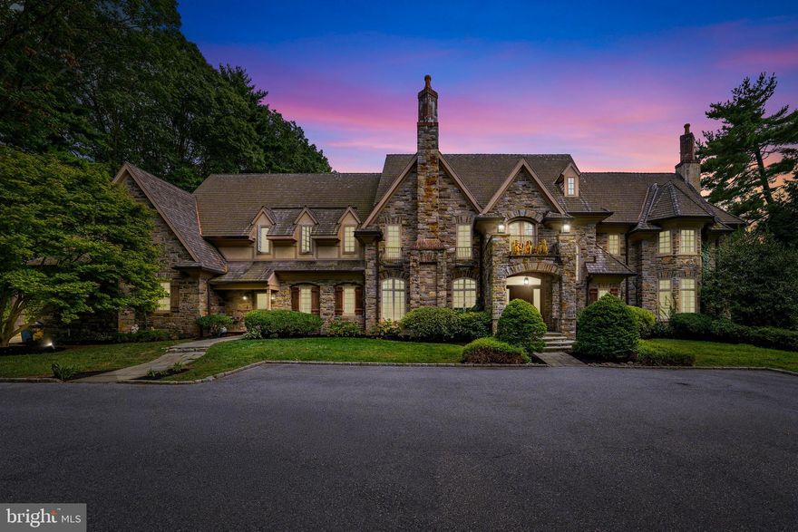 Set behind private gates on 1.61 acres, this magnificent 10,488 sq ft Bryn Mawr Estate blends old-world craftsmanship with modern luxury. Masterfully built by Michael Cutler Builders and designed by Scott McIntyre, the Stone Manor showcases soaring 10+ ft ceilings, walnut hardwood floors, an elevator, and grand proportions throughout its 5 Bedrooms, 7 Full Baths, and 2 Powder Rooms. A gracious courtyard leads to a marble foyer and formal living room with coffered ceilings and a gas fireplace. Additional highlights include a sun-filled conservatory, richly paneled library with Halkett millwork and French doors to the patio, and an elegant dining room with a gas fireplace and butler’s pantry. At the heart of the home, the Clive Christian gourmet kitchen features a walk-in pantry, Sub-Zero refrigerators and freezer, Wolf range, double ovens, and a breakfast area opening to the family room dark wood coiffured ceiling and  stone fireplace creating a warm and cozy ambiance. A mudroom with cubbies and two powder rooms complete this level. The primary suite retreat offers dual walk-in closets, two spa-like baths with marble finishes, a sitting room with a fireplace, and a private balcony overlooking the grounds. Four additional en suite bedrooms and a cedar closet complete the second level. The walkout lower level is designed for entertainment and wellness with a theater, gym, sauna, spa, wine cellar, second kitchen, and family room.  Exceptional details include a Lutron lighting system, custom shutters, a whole-house generator, an irrigation system, a 3-car garage, and a walk-up attic. Outdoor living is enhanced by a rear patio with a stone fireplace—ideal for year-round gatherings. Located on one of the Main Line’s most prestigious streets in the award-winning Lower Merion School District, this estate offers unmatched elegance, privacy, and convenience—just minutes to the R5 train, dining, and Center City.